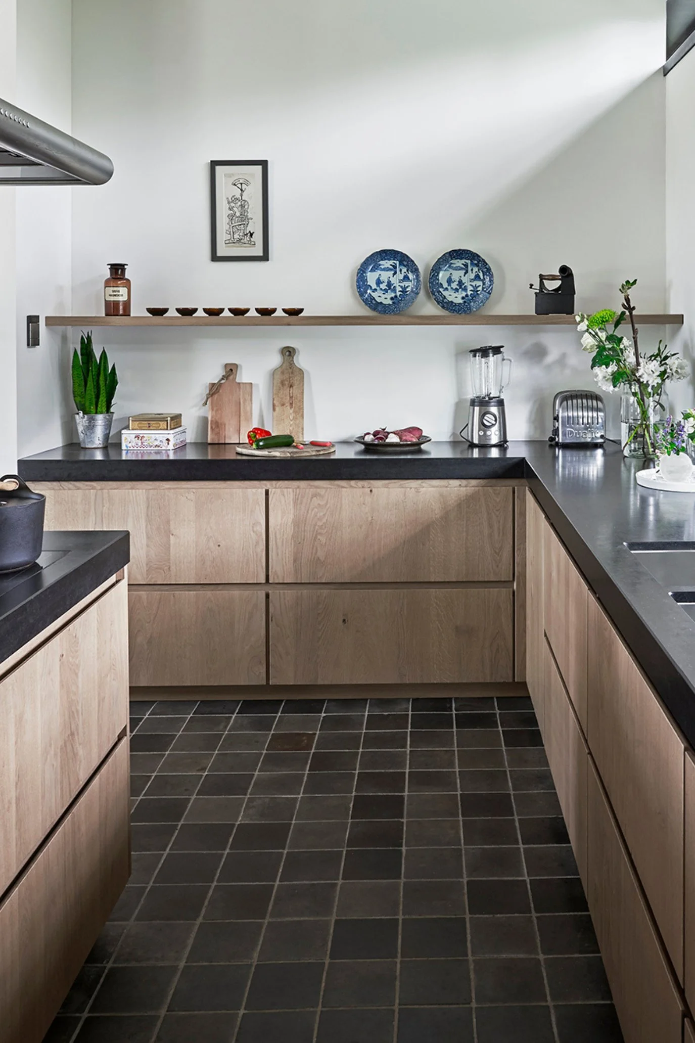 A modern kitchen with kitchen items like a toaster, juicer and chopping boards on the work top and a row of six small dishes next to two Delft Blue plates on the shelf