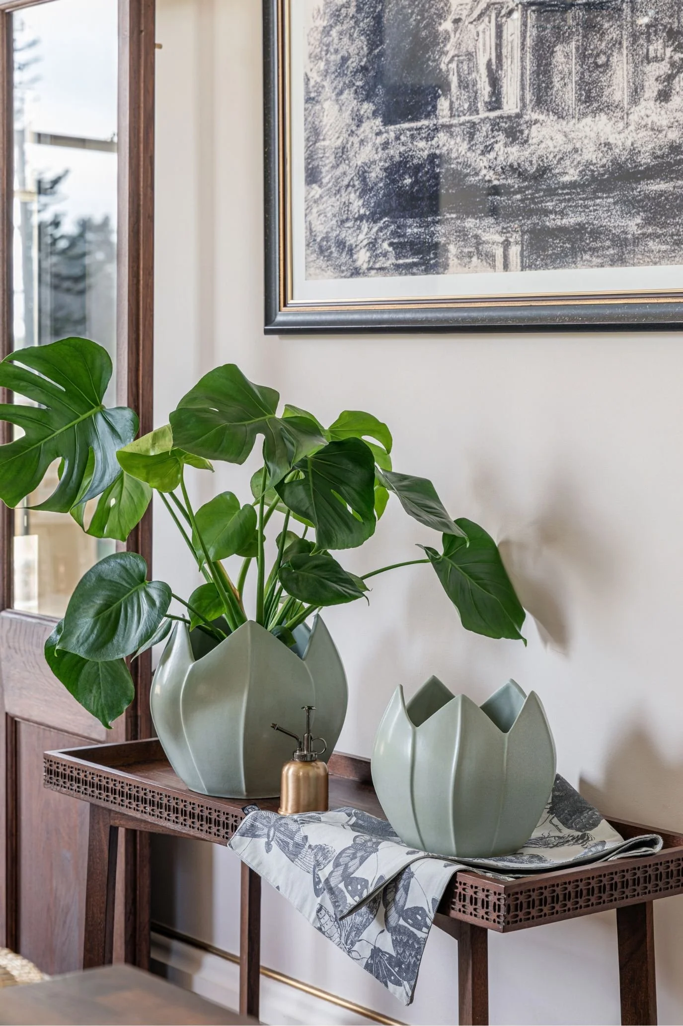 Pistachio green flower-shaped planters on a wooden console, with a leafy houseplant beneath framed artwork.