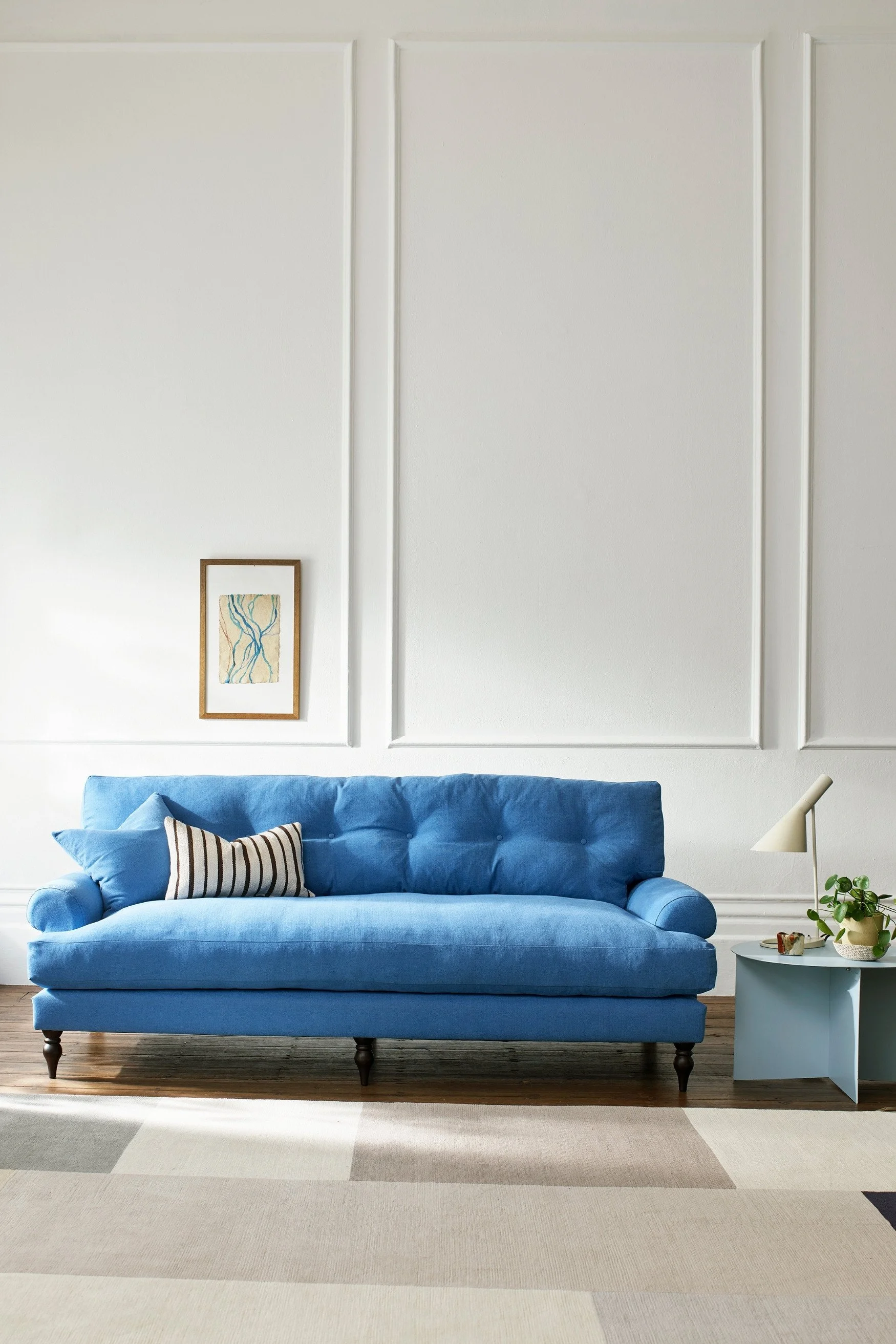A blue sofa with a black and white cushion against a white panelled wall with a small pale blue table next to it.