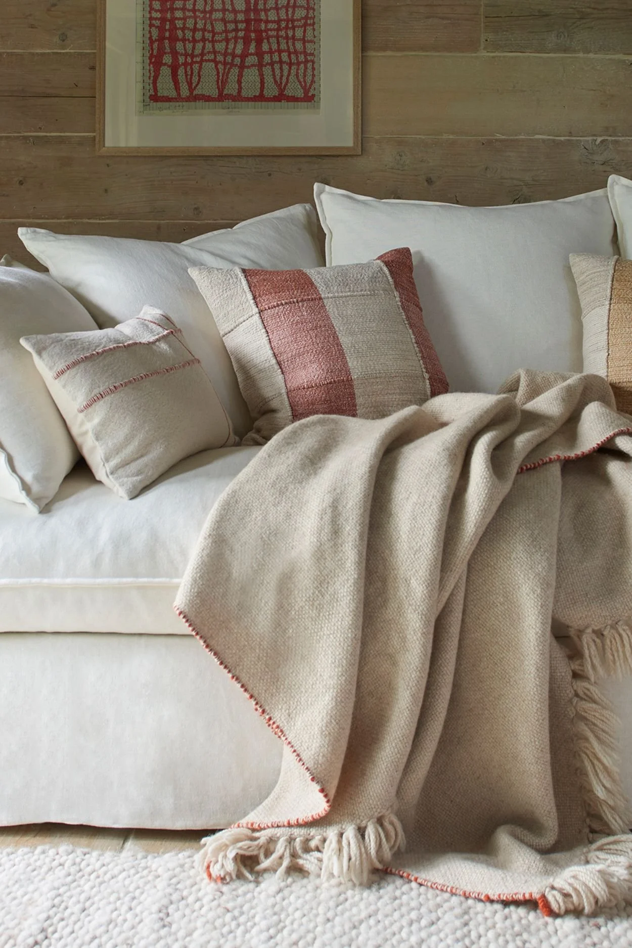 Home decor items stylish throw on a cream linen sofa with cushions in cream and earthy colours set against a rustic wood clad wall