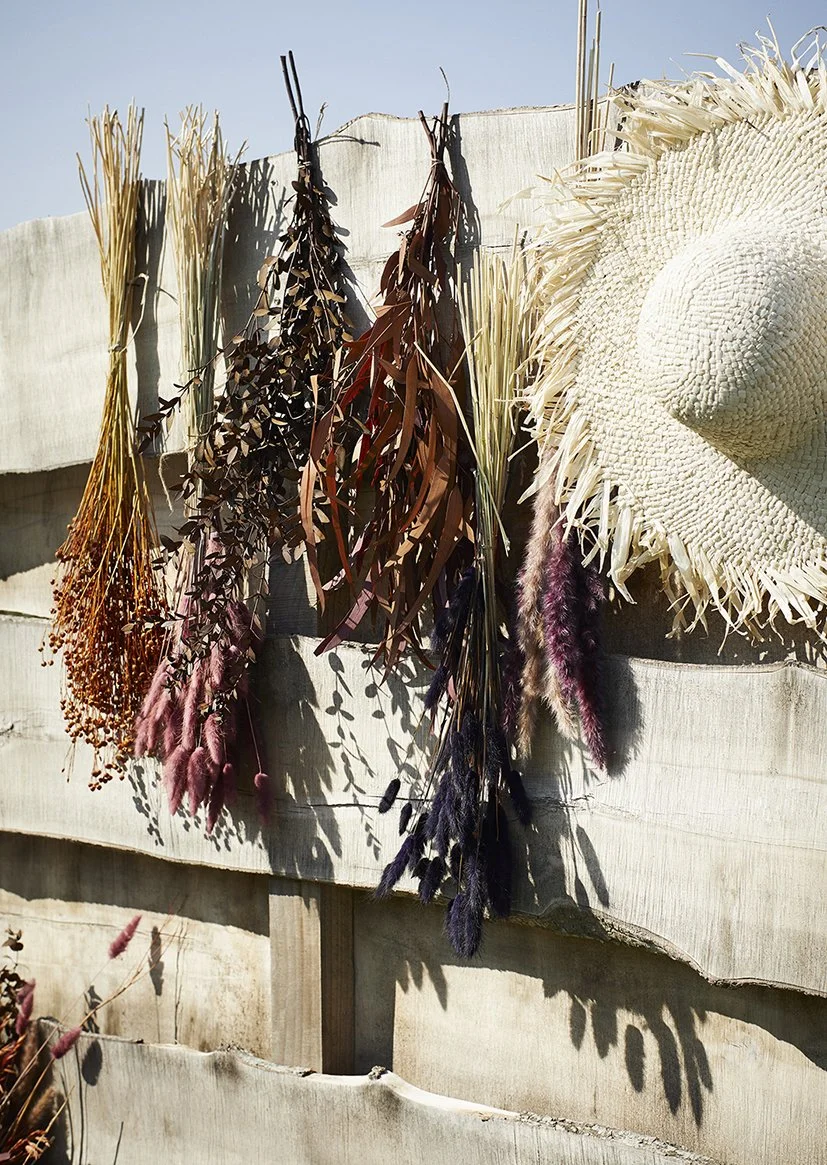 Dried grasses and leaves-Eucalyptus Stems hanging upside down against a wall next a straw sunhat