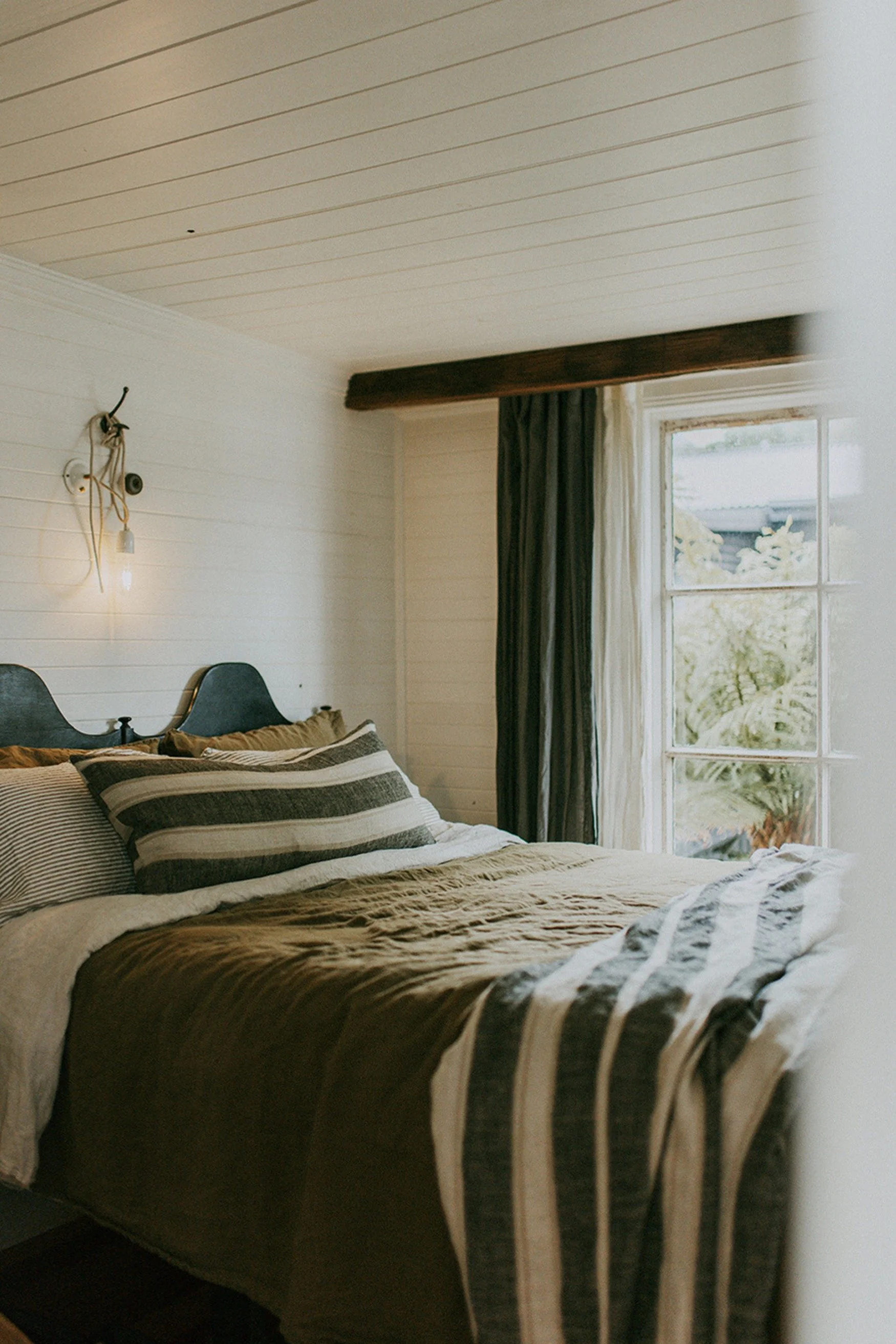 A bedroom with green and off-white bedlinen, a dark green headboard and green curtains
