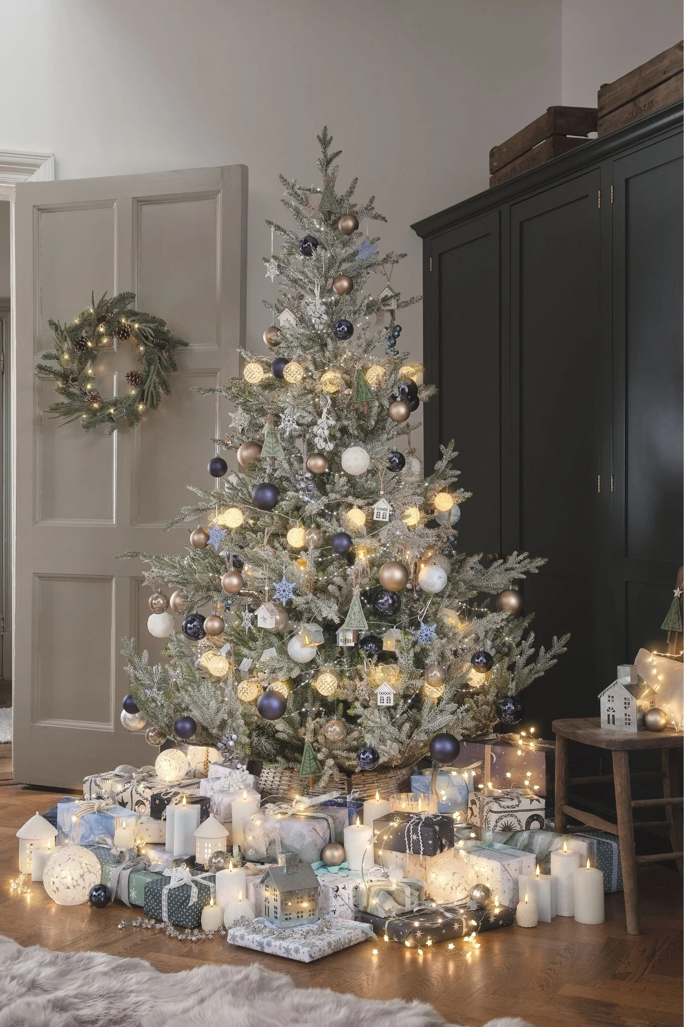Frosted Christmas tree with blue and white ornaments, warm lights and illuminated miniature houses around the base.