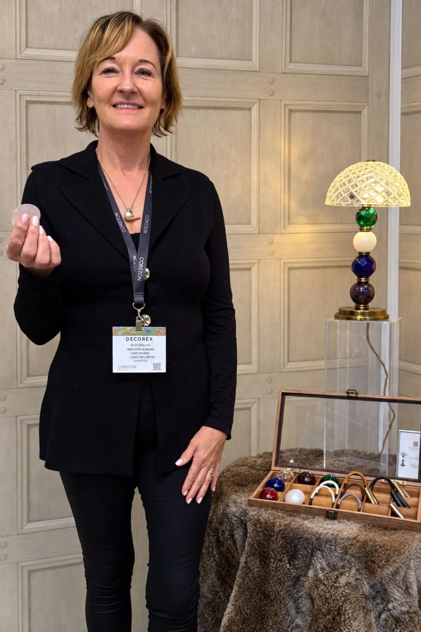 Lighting designer beside a bespoke table lamp with oversized colourful jewel details beneath a pale shade.