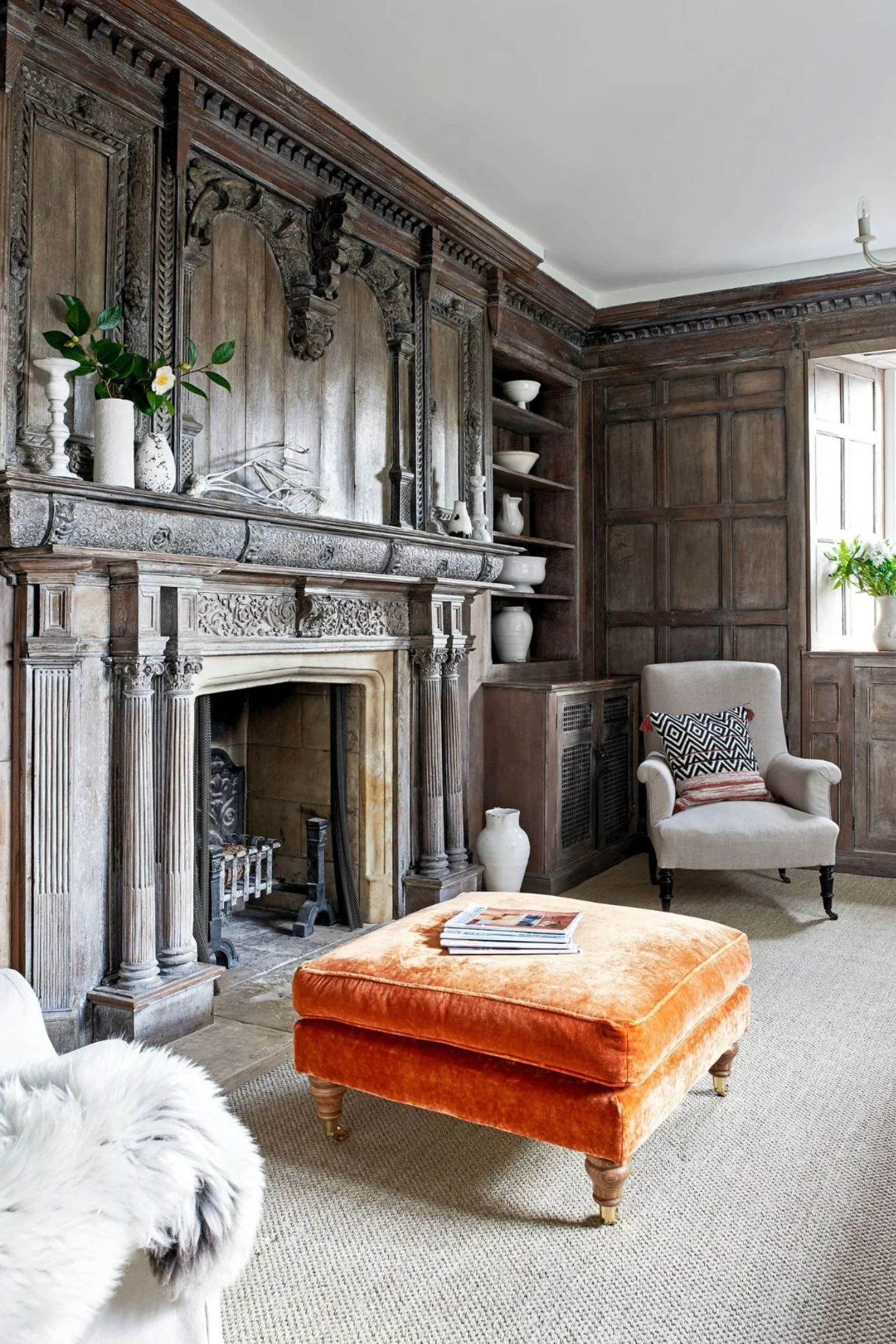 Traditional English manor drawing room with dark wood panelling, linen sofa, vintage ceramics and burnt orange velvet ottoman.