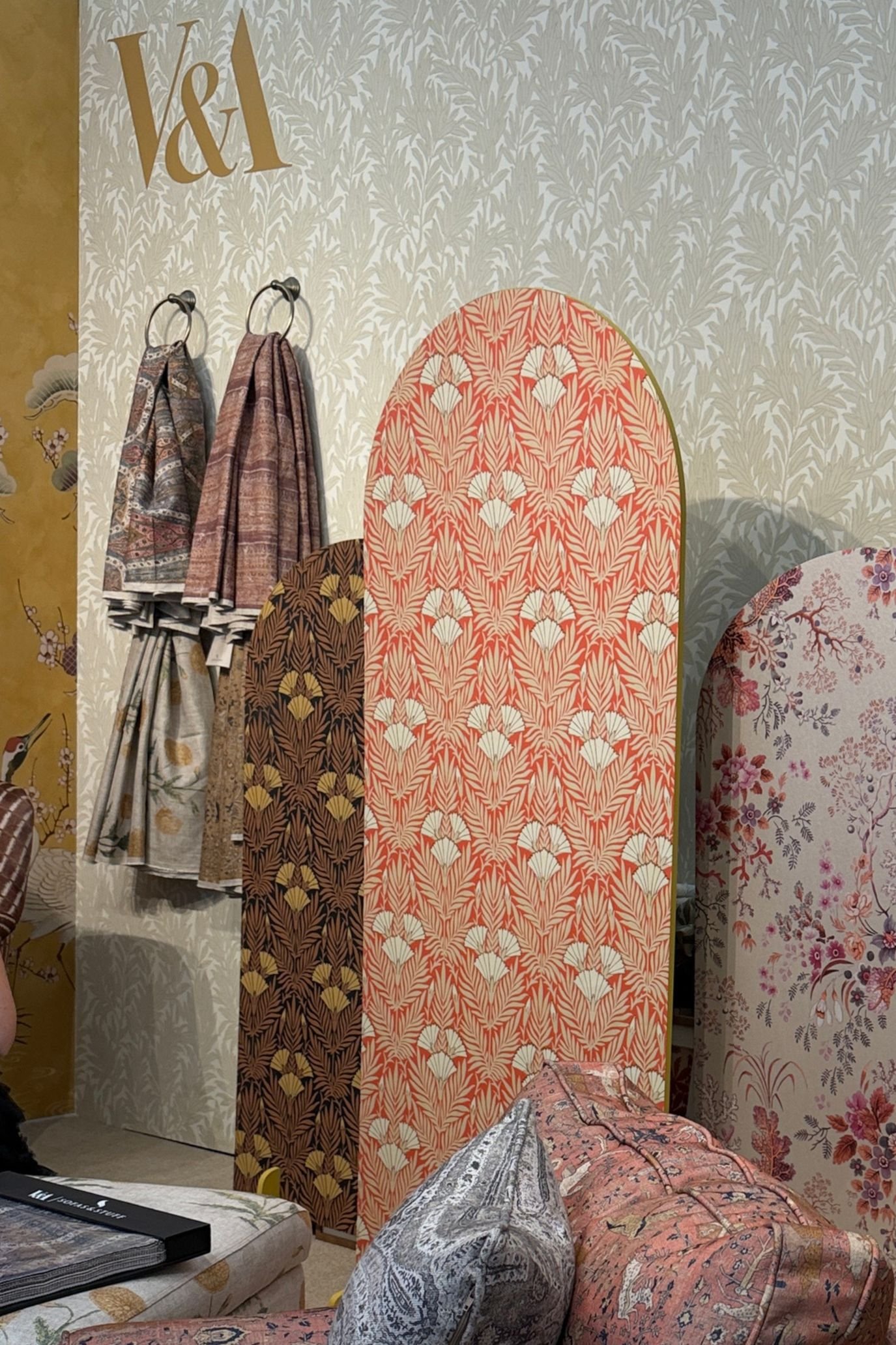 V&A display of heritage-inspired floral fabrics and wallpapers in coral, cream and muted green tones.
