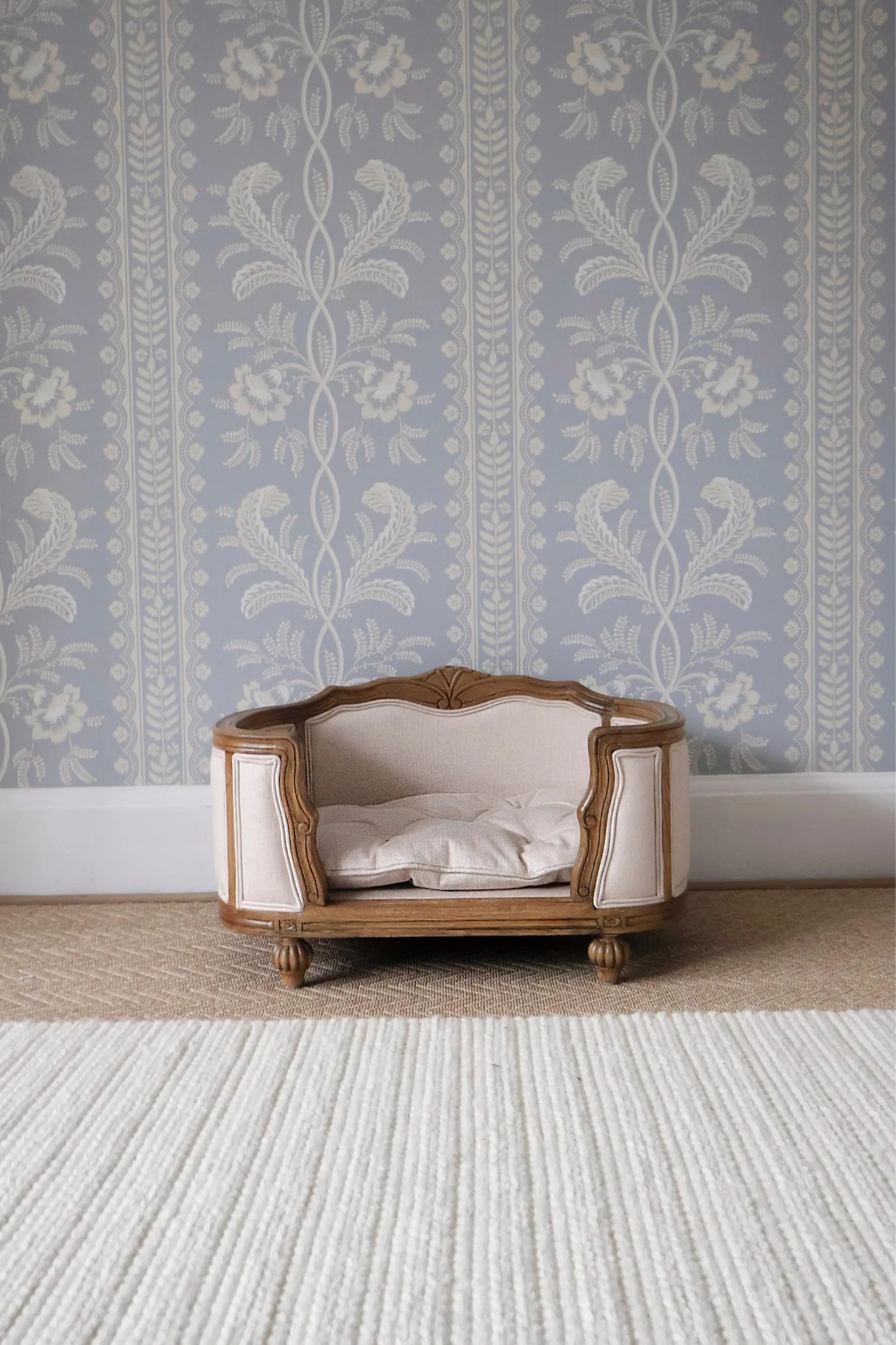 Antique-style wooden dog bed with carved frame and neutral linen upholstery.