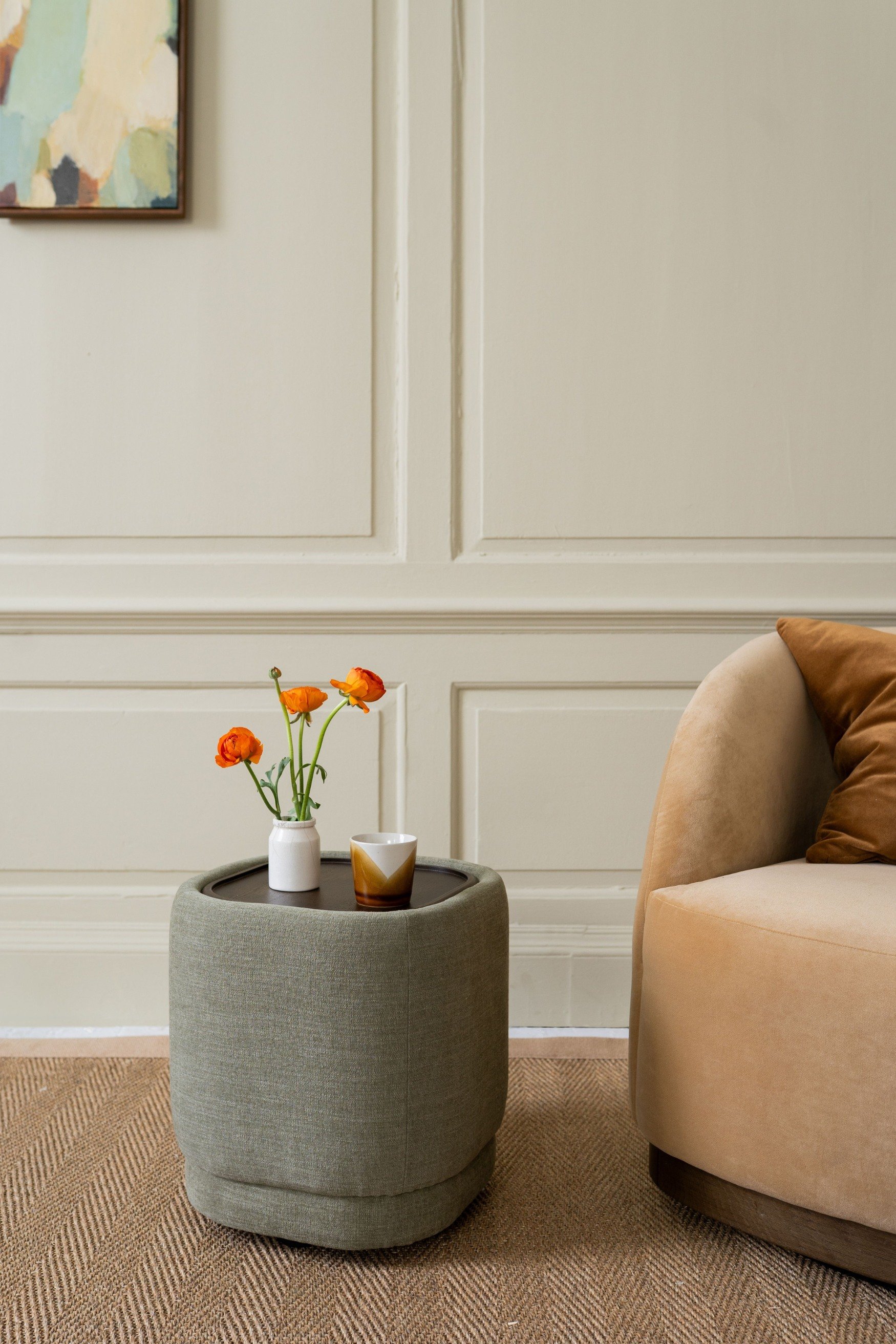 A fabric covered side table with a small white pot and three orange flowers
