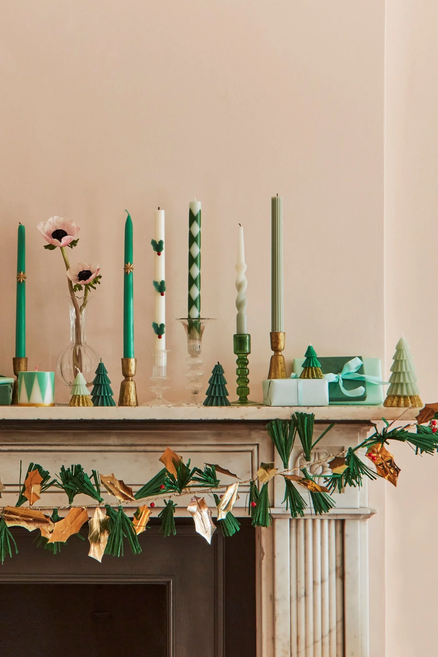 Styling with candles a mantlepiece with several tapered green and white candles as well as candles in the shape of Christmas trees and drums
