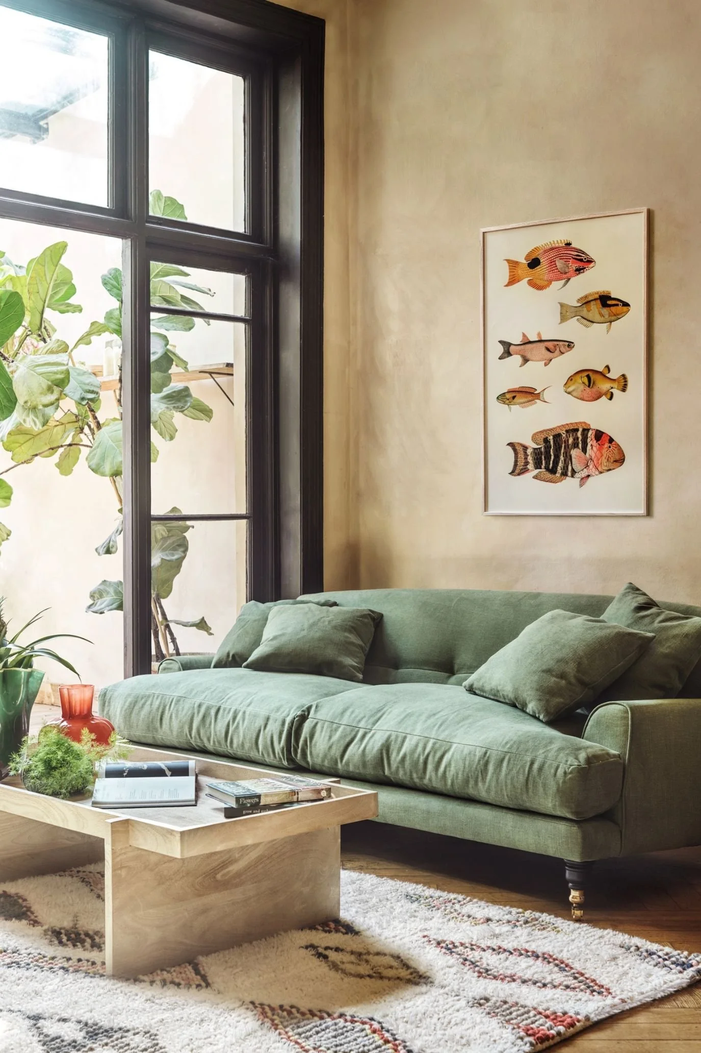 Olive green sofa with matching cushions beside a large window, paired with a wooden coffee table and patterned rug.