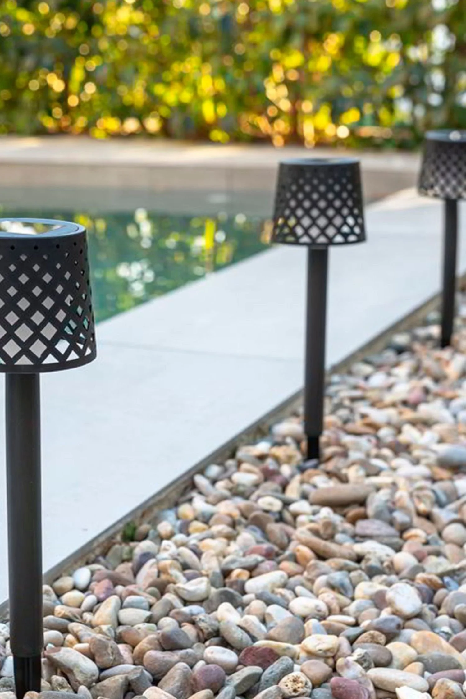 Solar spike lights lining a garden pathway beside a swimming pool, creating warm and stylish outdoor lighting.