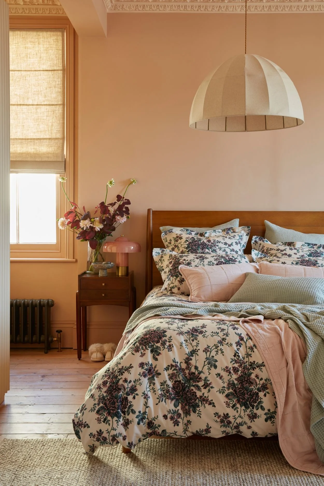 A bedroom with a large linen pendant above a bed with floral blue and white linen and throws and cushions in light green and pink