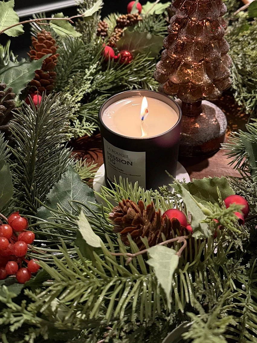 A lit scented candle surrounded by fir, holly and berries
