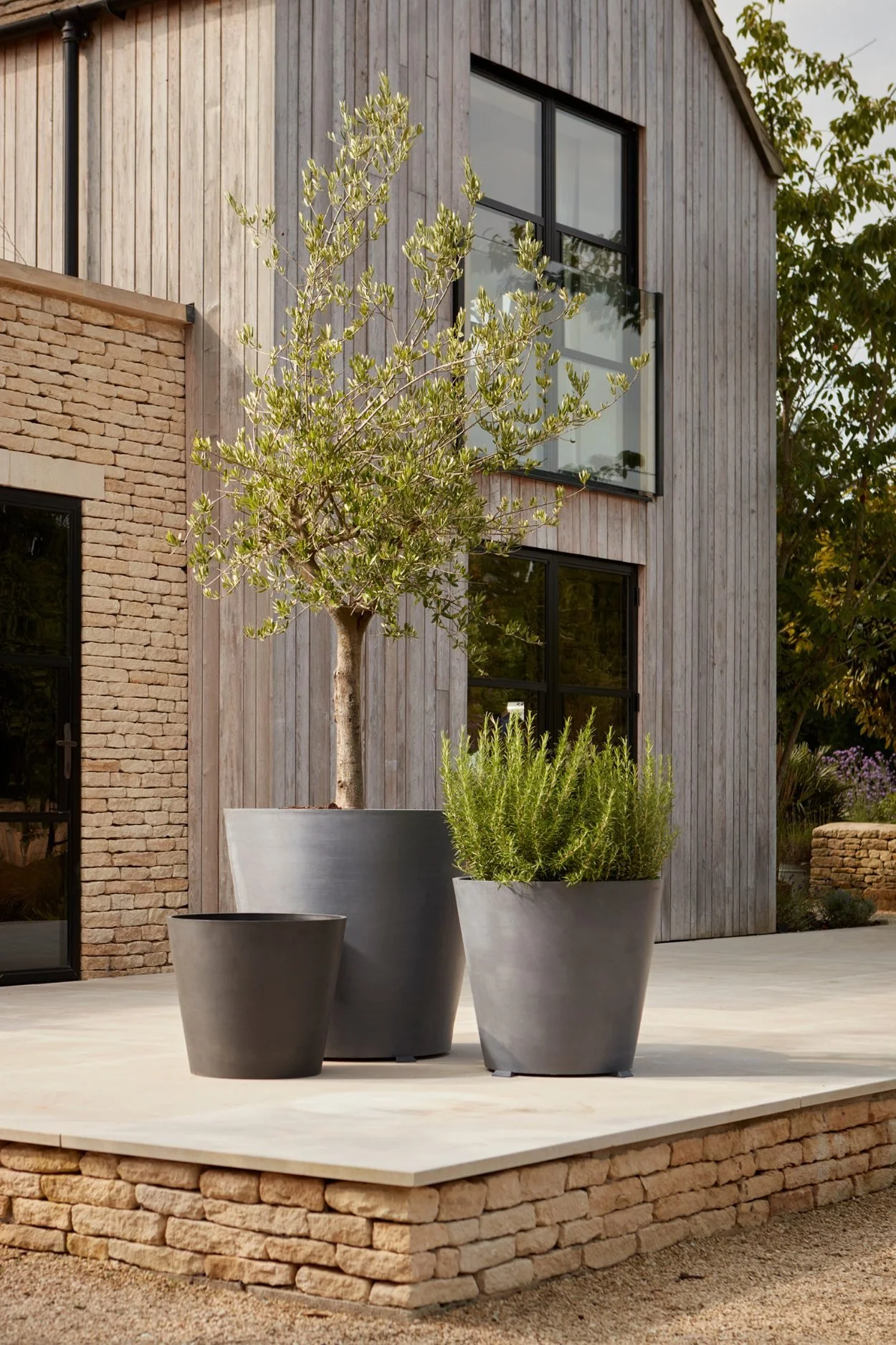 Large dark grey recycled plastic planter containing a tree next to two smaller pots