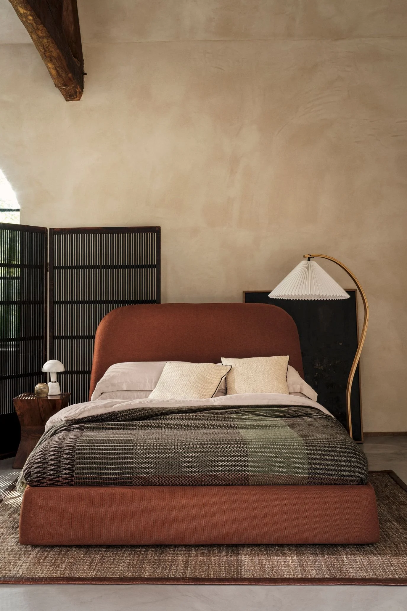 Upholstered bed with a curved terracotta headboard and layered bedding