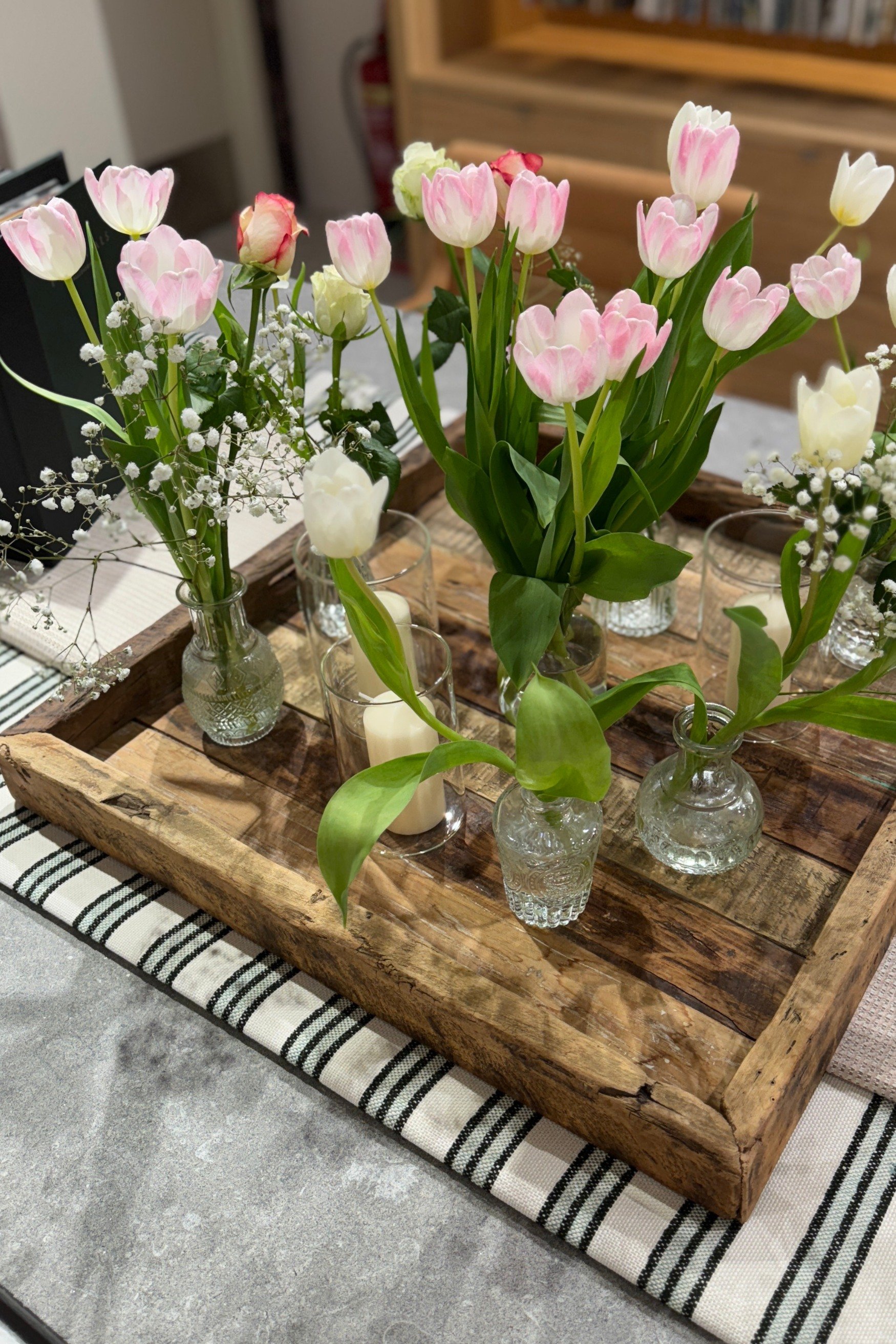 A wooden tray filled with bud vases all with tulips in pink and gypsophila