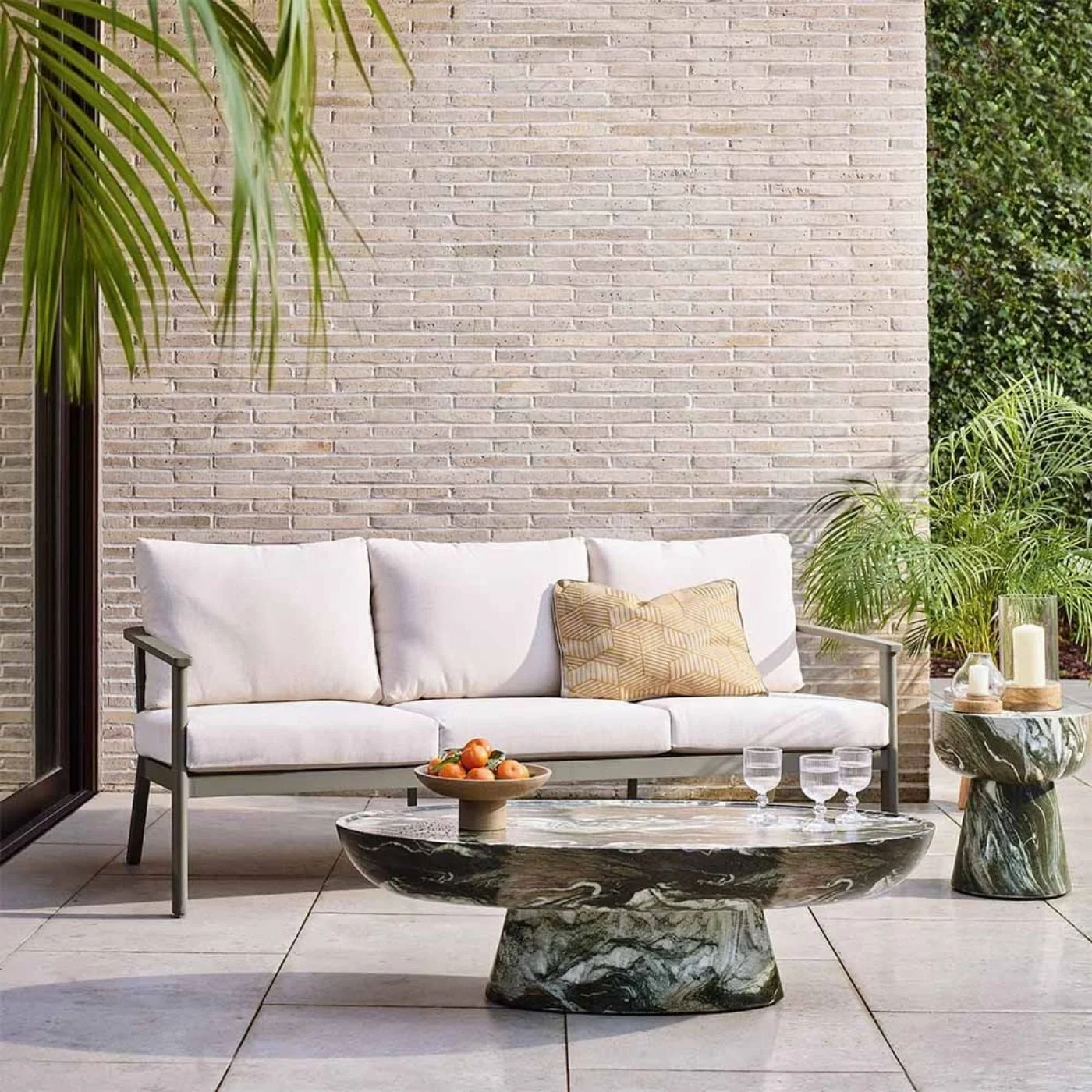 A sage green and cream outdoor styled with a yellow geometric cushion in a setting with a green marble coffee and side tablef