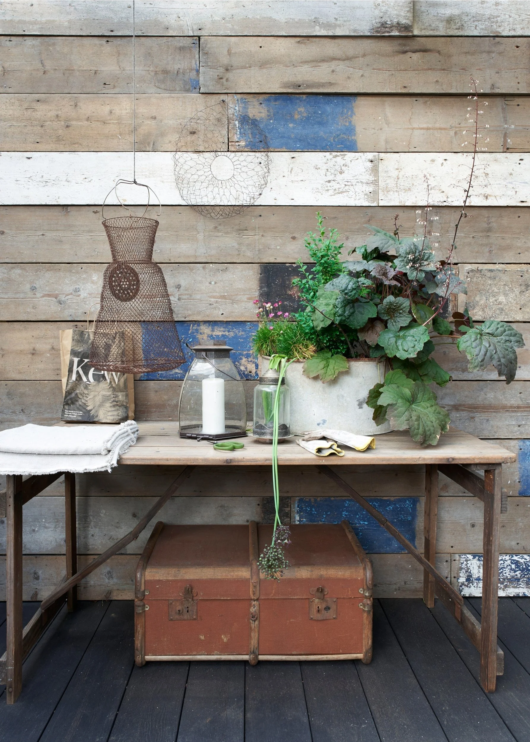an outdoor console table with potted plants , a wire dress, lanterns set against a rustic reclaimed wood wall