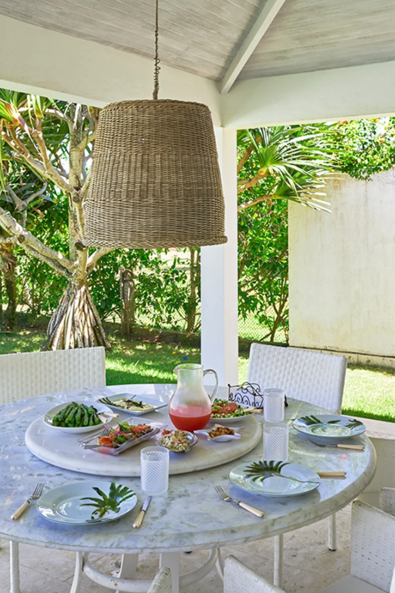 Covered outdoor dining area with round marble table, Lazy Susan and oversized woven rattan pendant light.