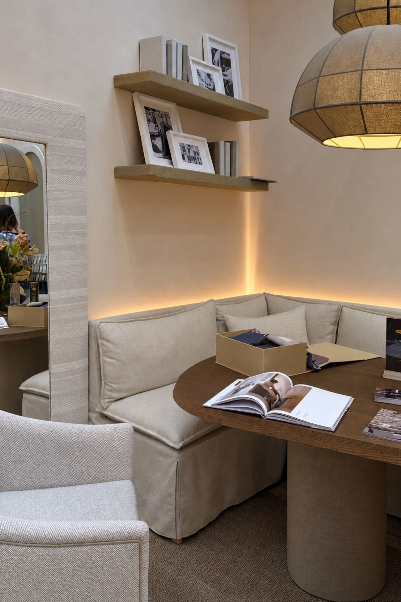 seating	Neutral upholstered corner seating beneath fabric-covered shelving, with concealed lighting and a small wooden table.