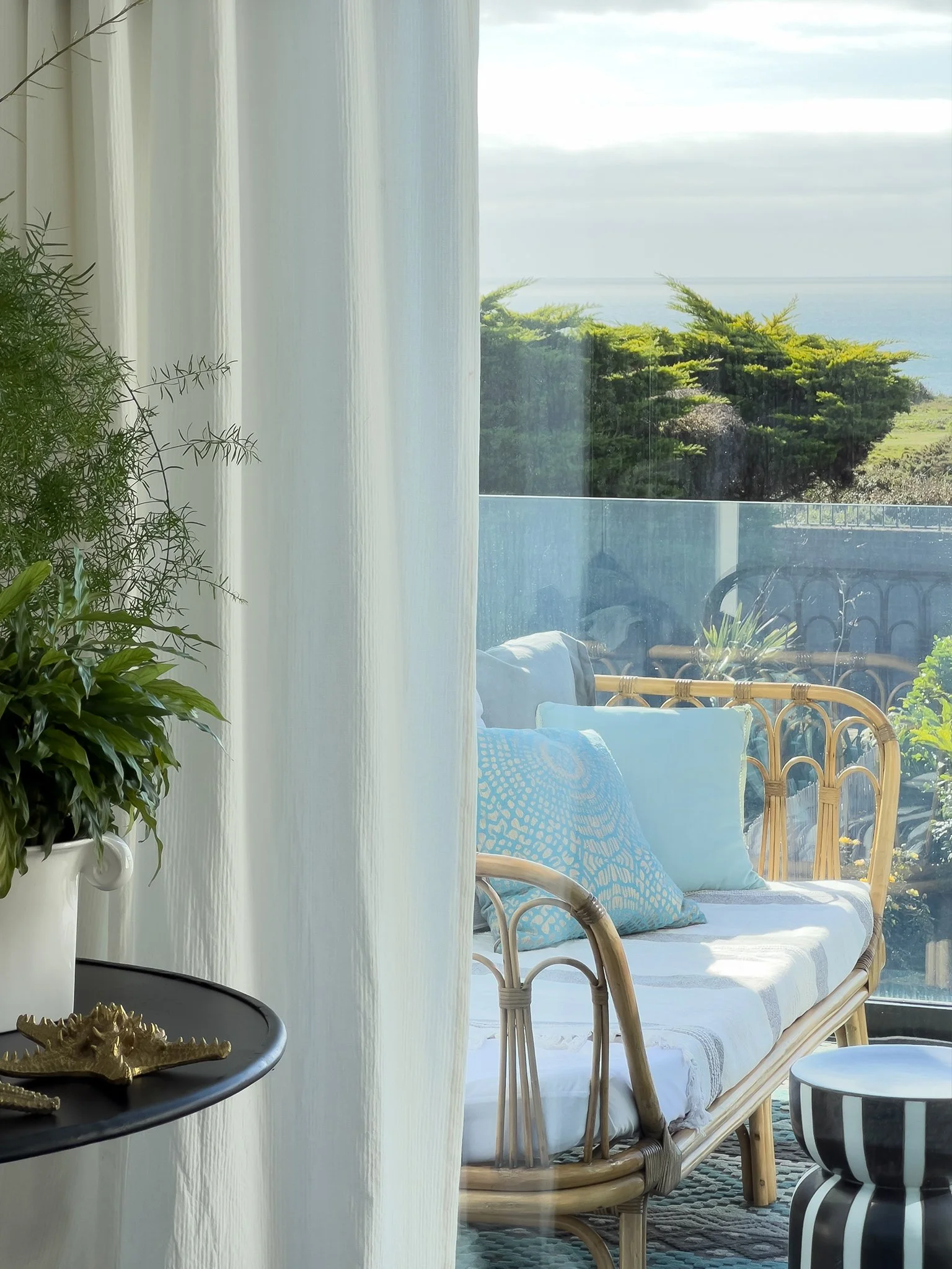 a balcony overlooking the sea with a bamboo day bed styled with aqua toned cushions.