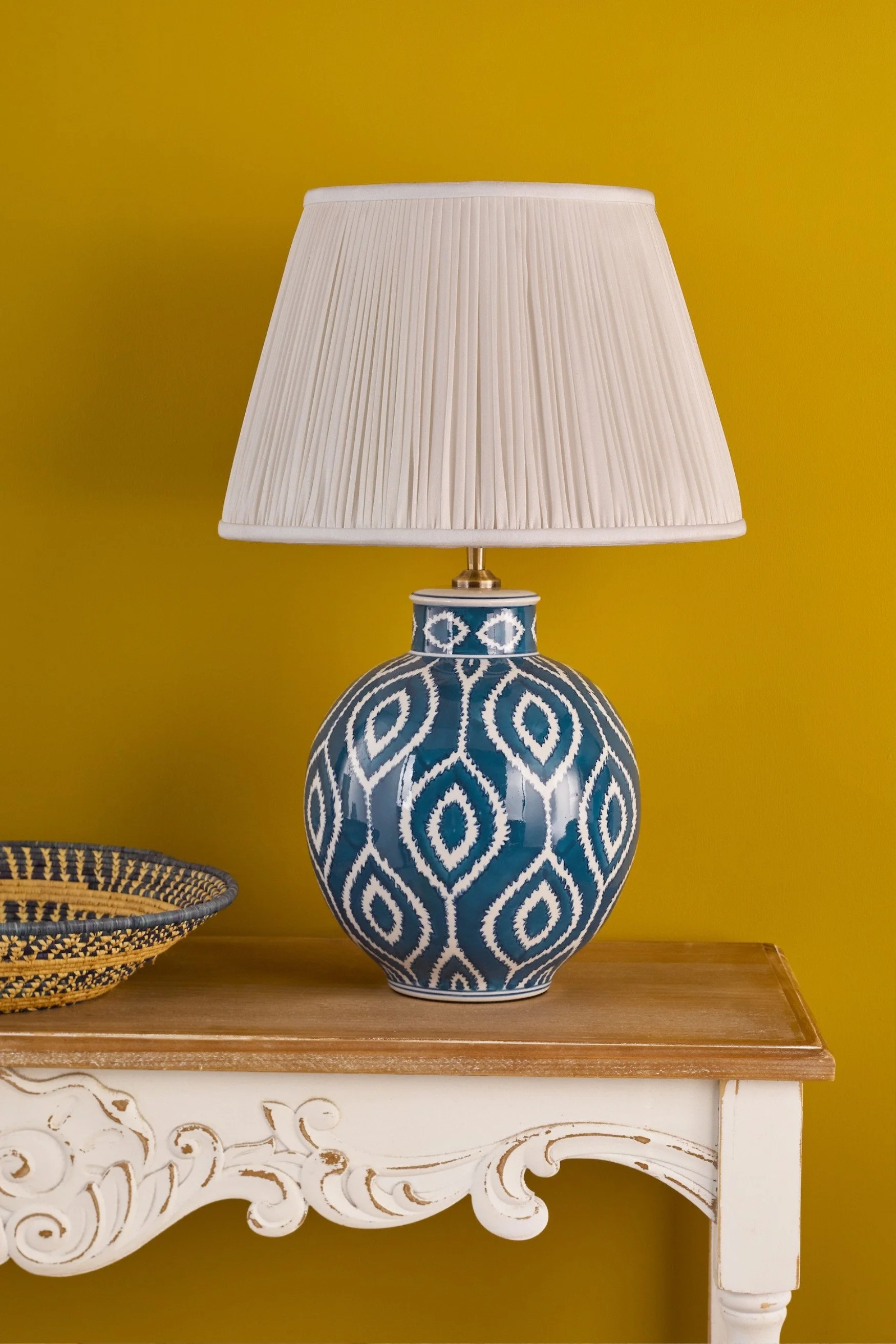 A blue ceramic lamp in a pattern against a yellow wall
