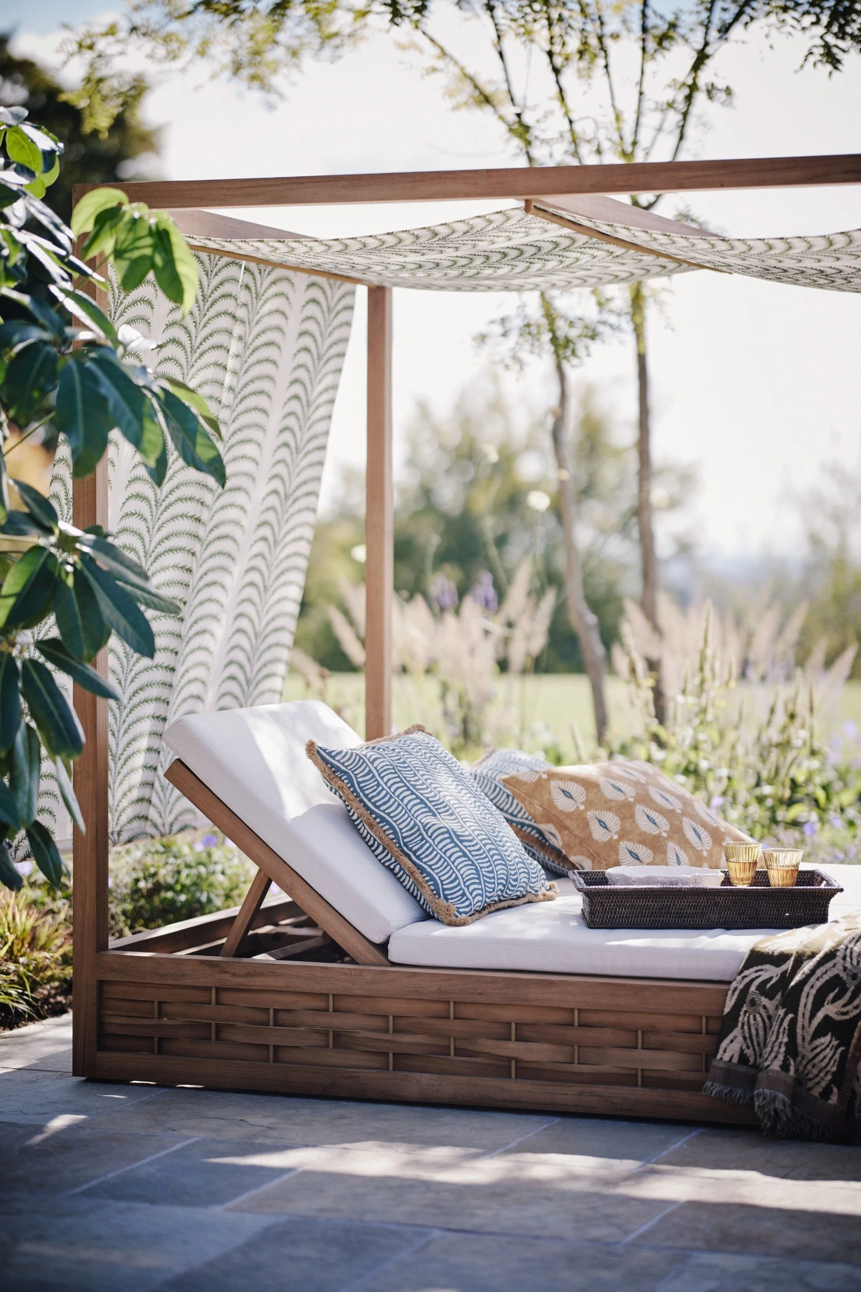 A day bed with a canopy in a garden with blue and yellow large outdoor cushions