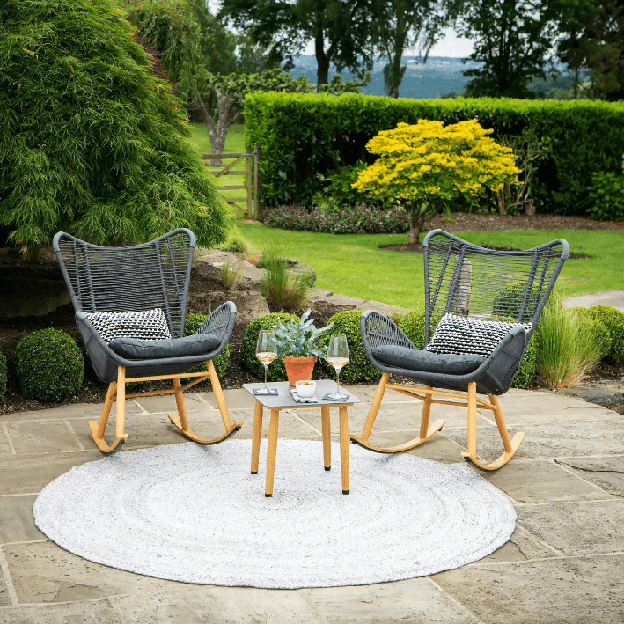 A patio with a circular outdoor rug, two chairs and a small table in a garden setting