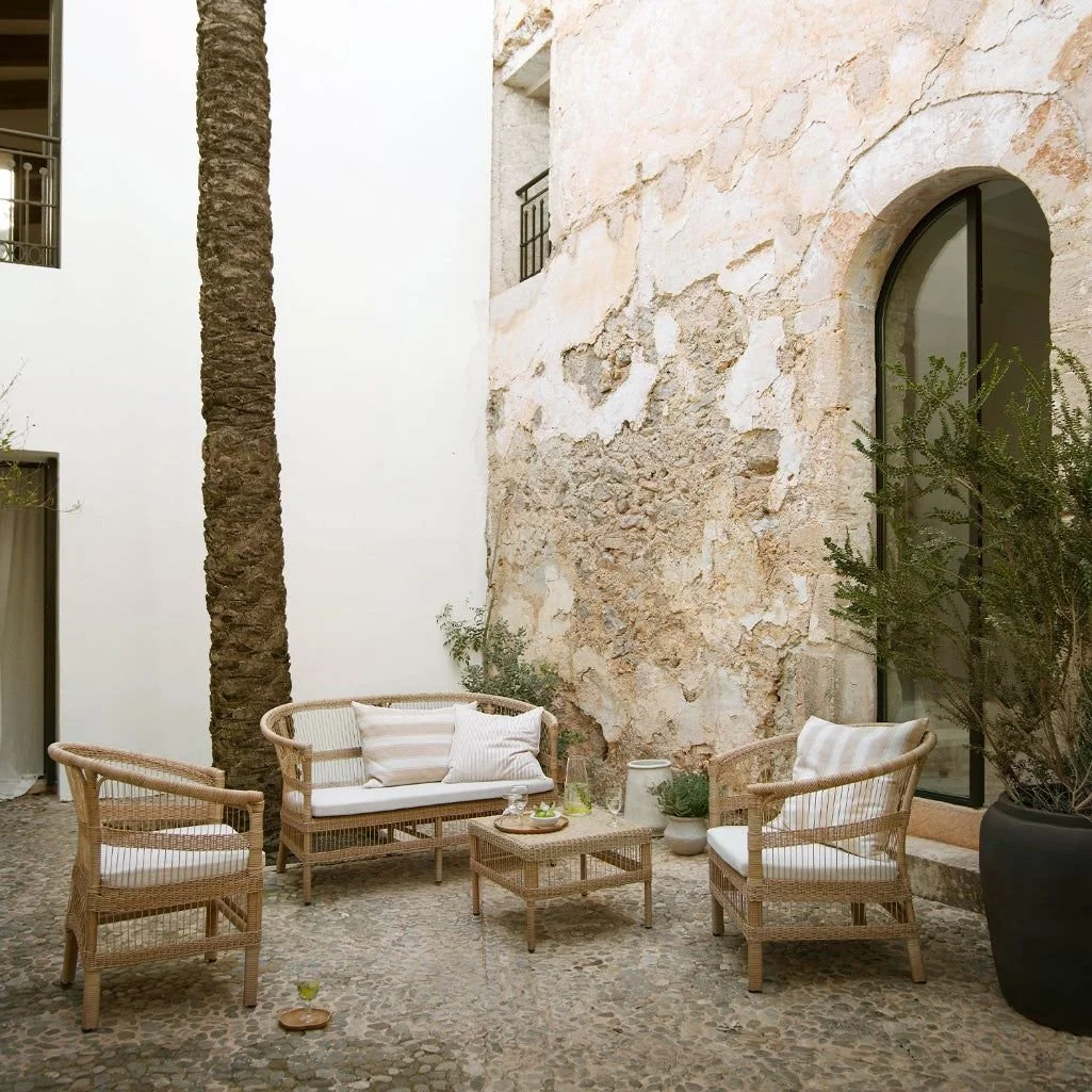 Outdoor wicker chairs and sofa with soft beige striped cushions in a stone courtyard