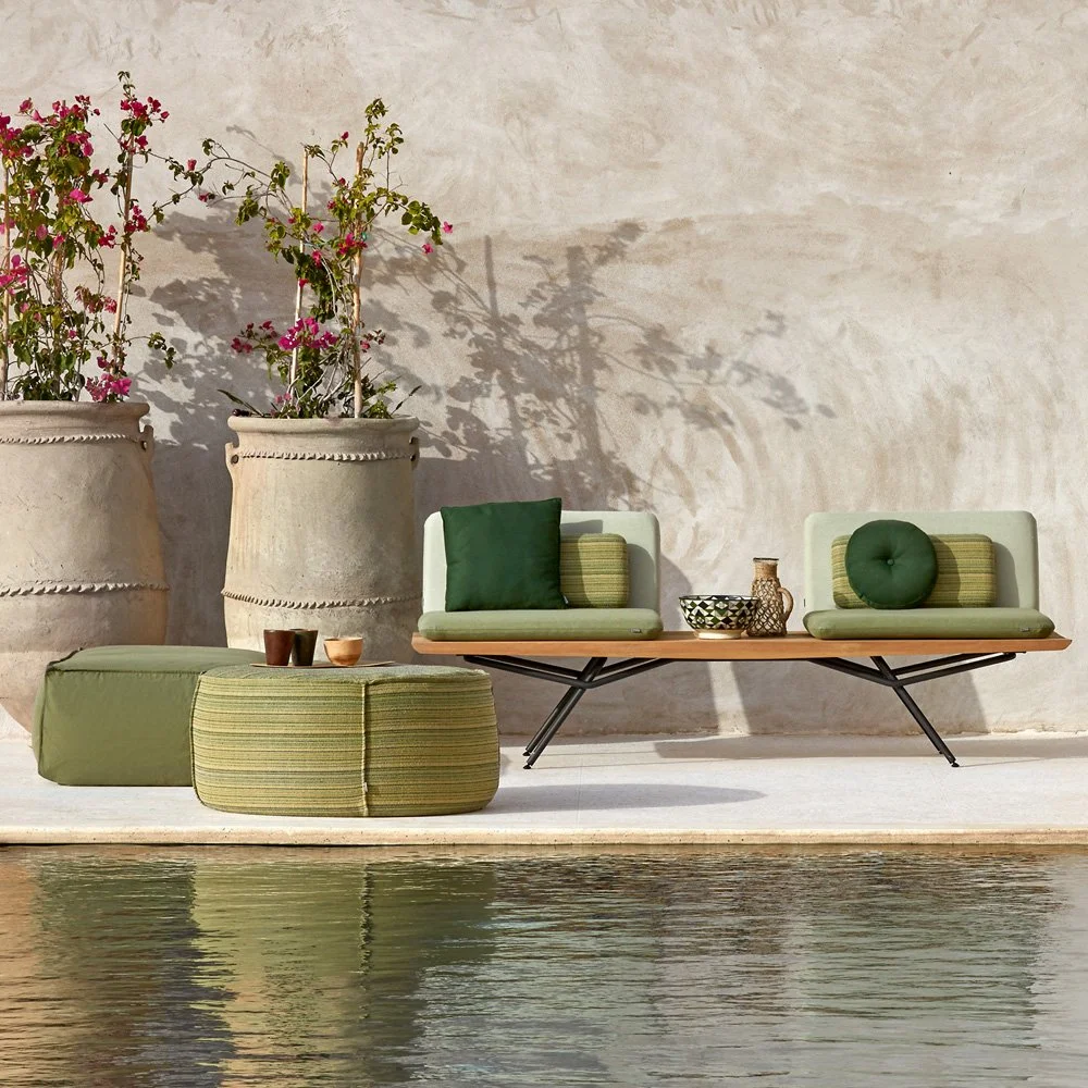 Outdoor lounge area with green cushions and pouffes by a plaster wall and pool
