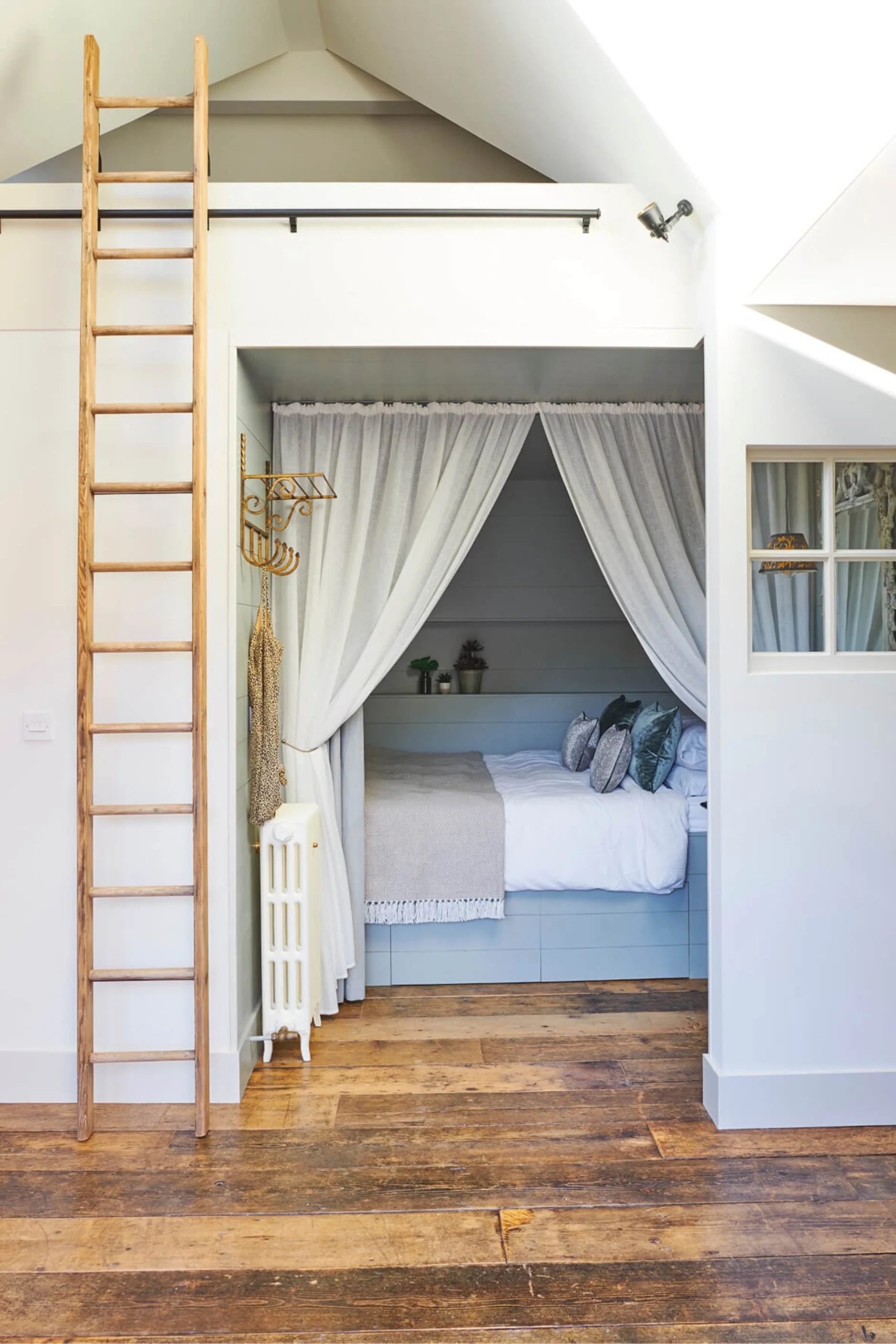 A bedroom with a mezzanine above and ladder  leaned against the wall