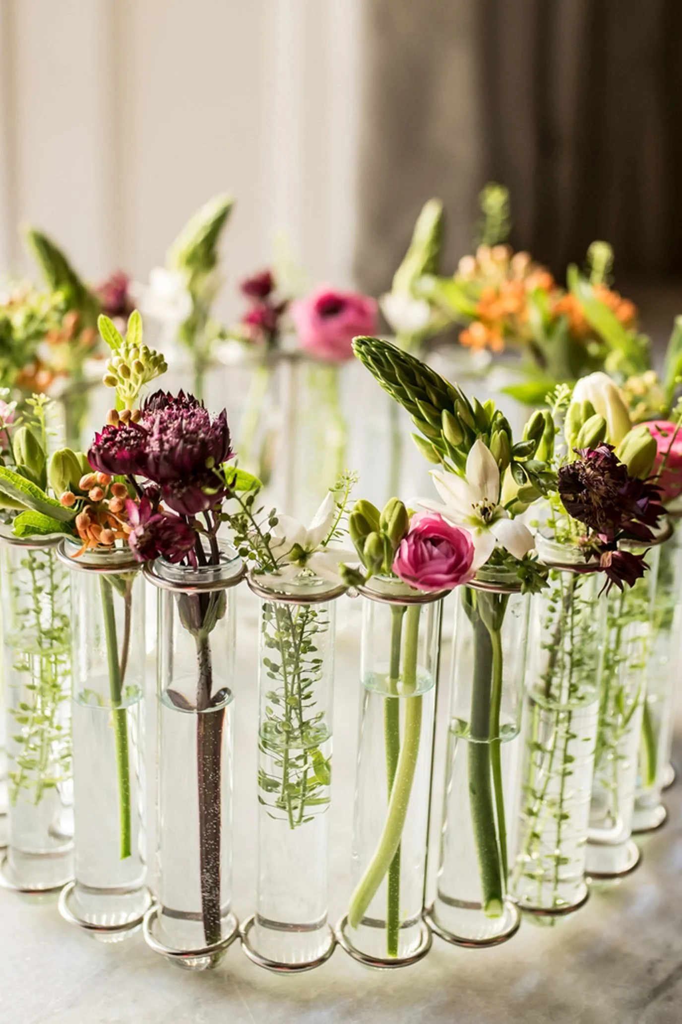 Linked clear glass test-tube bud vases displaying individual flower stems. Silver handbag vase