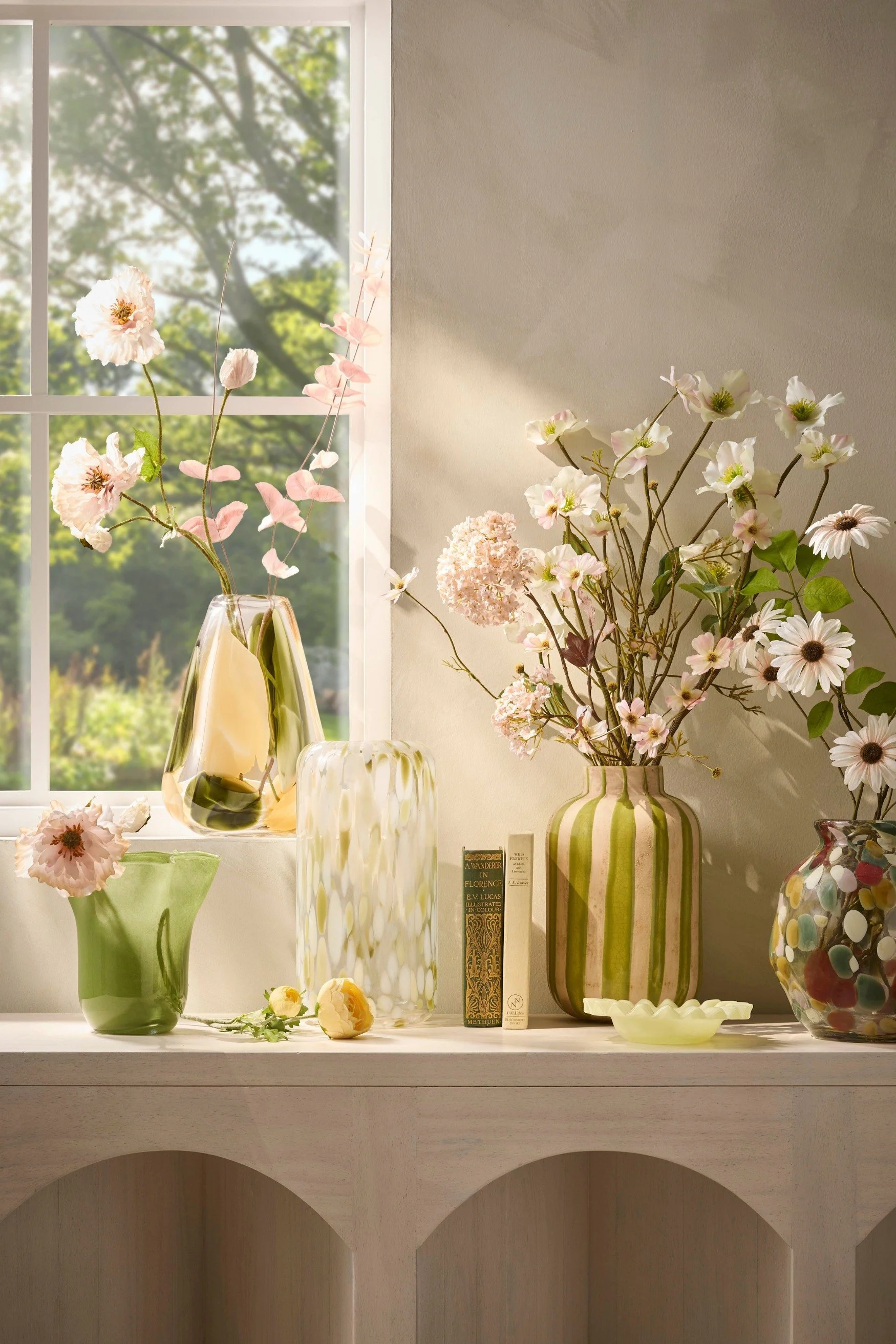 A mix of five different vases in different soft pale colours with artificial flowers in them