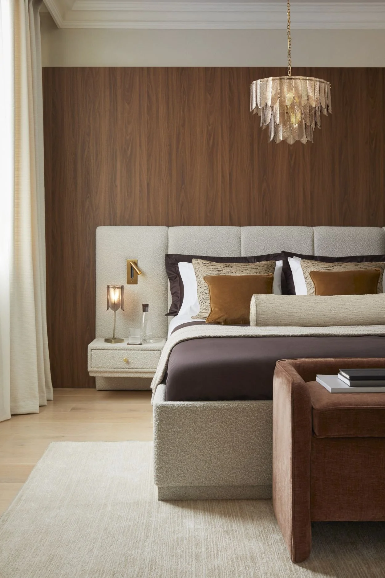 A bedroom with a wood wall and cream fabric extended headboard and cream curtains
