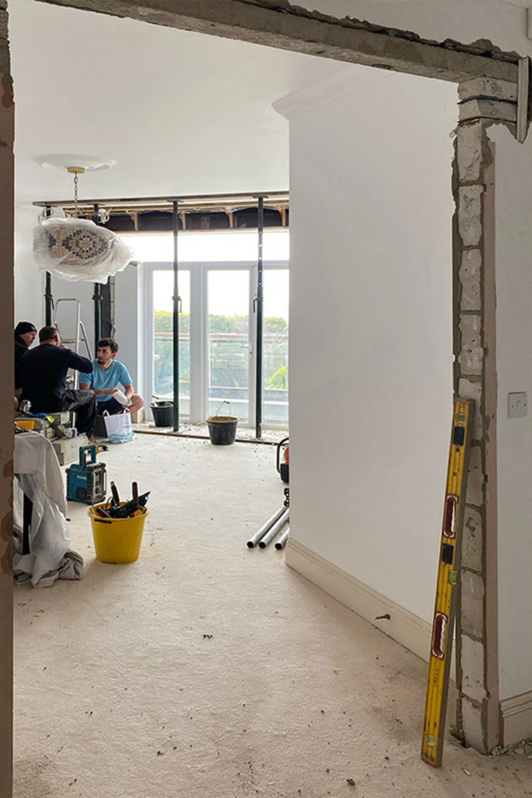 Dining room with doors knocked out, white walls and builders sitting