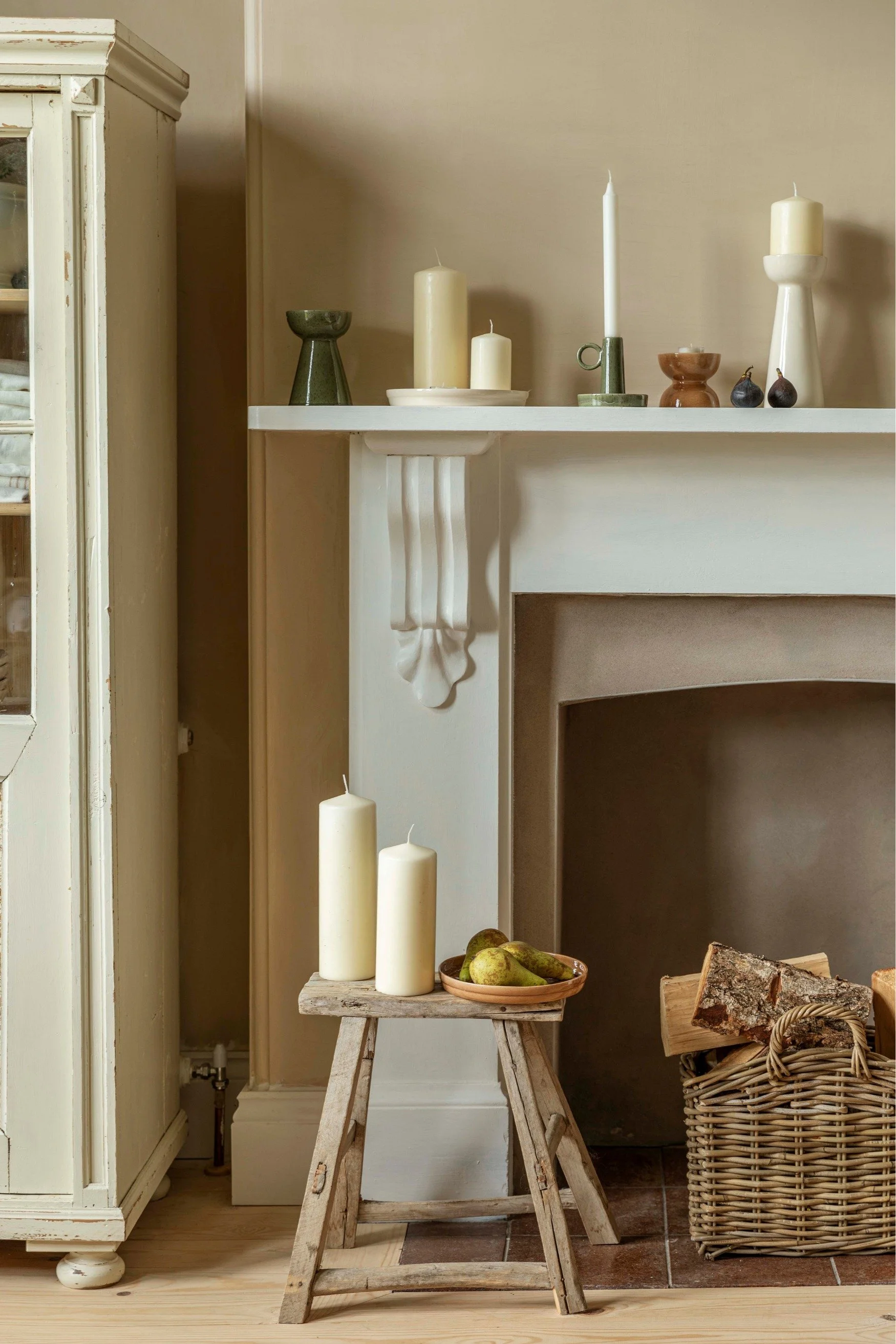 A mantelpiece with a bunch of different candle holders in green, brown and cream with different size candles