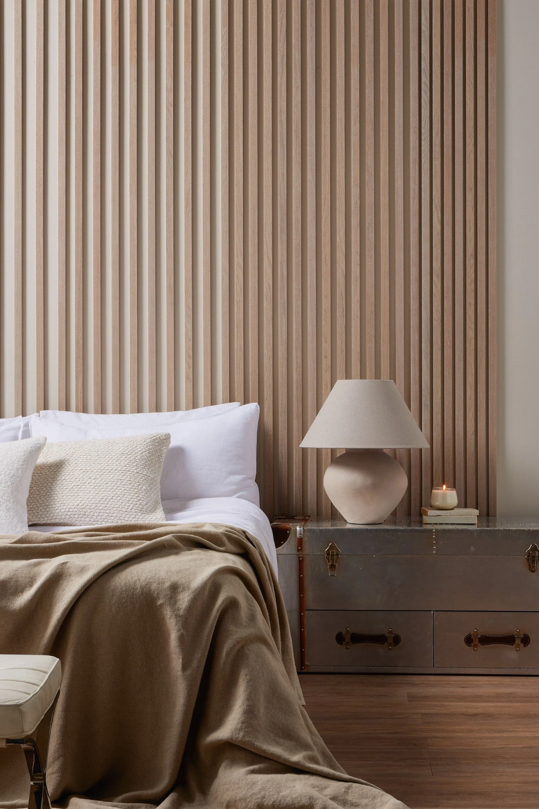 A wall made of slated wood acting as a headboard next to a lamp and bed