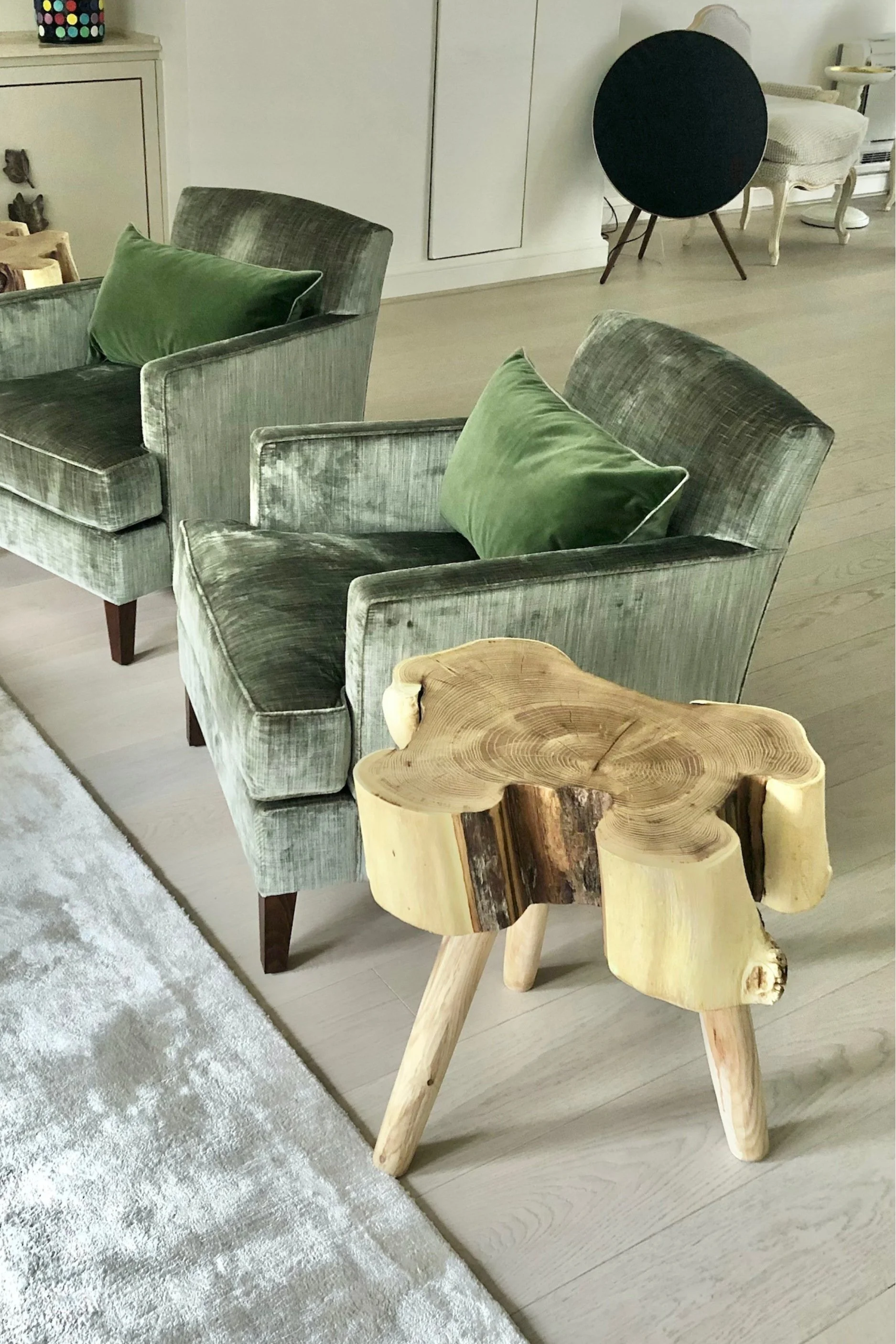 a wooden handmade tree trunk table with legs next to two velvet green chairs with green cushions