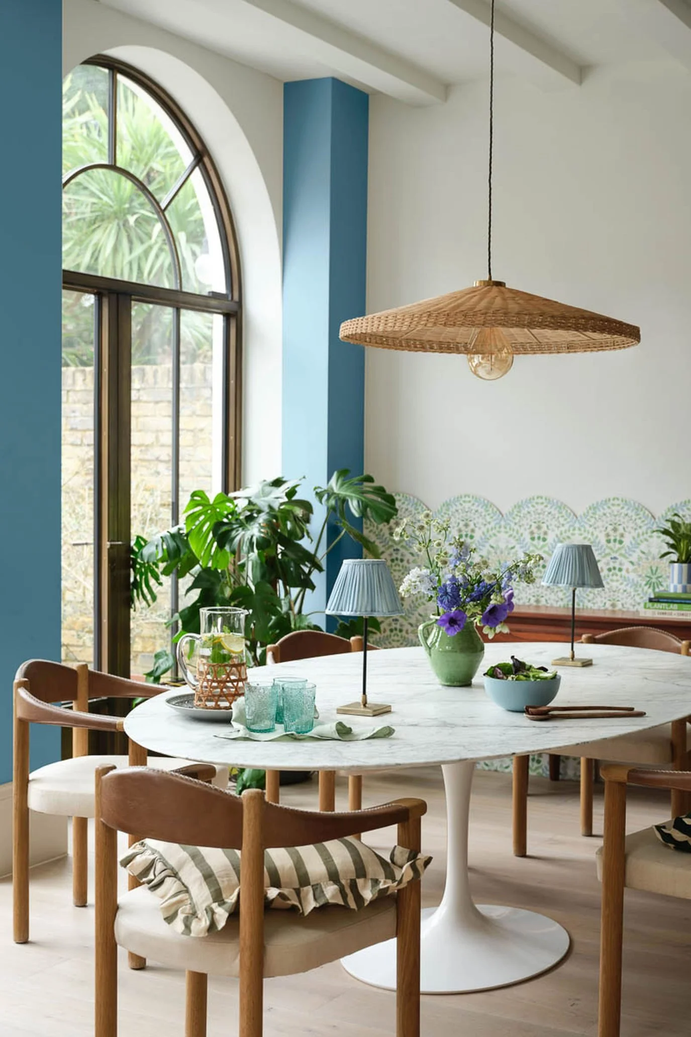 a dining room with blue accents, an oval dining table and two portable lamps with a large rattan pendant hanging above