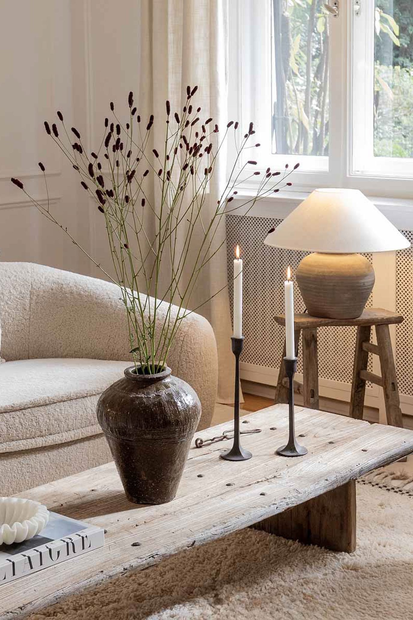 Antique brown glazed stoneware vase styled with tall dried stems on a rustic coffee table in an Organic Modern living room.