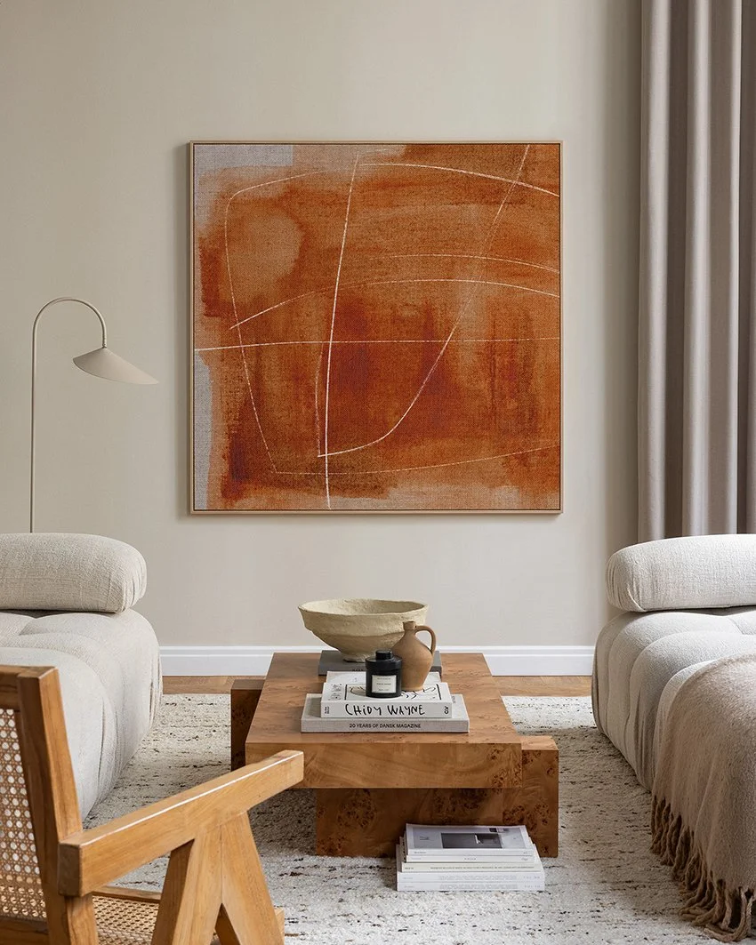 A living room with burnt orange abstract artwork on a beige wall with cream sofas either side