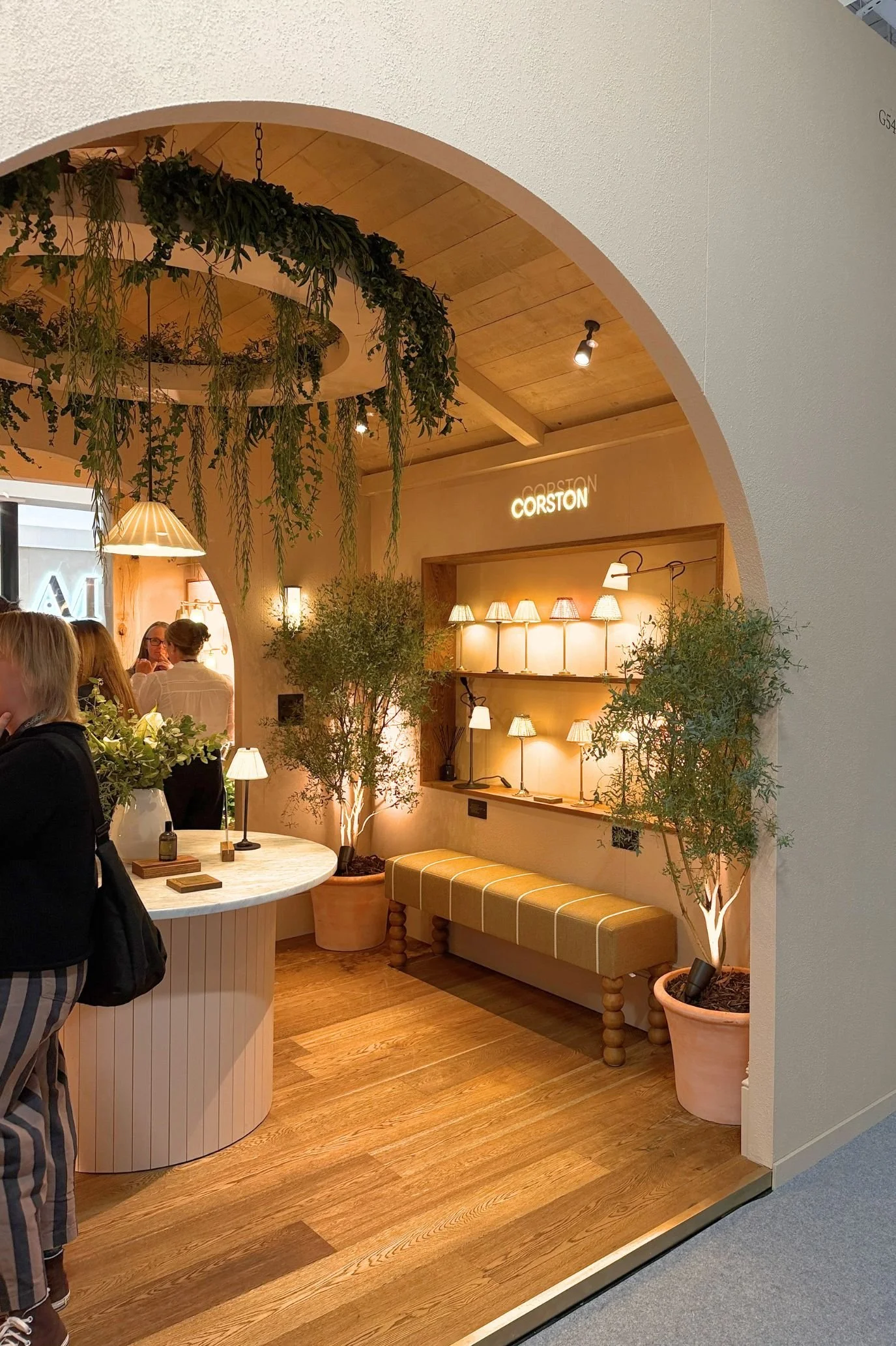 Arched entrance to the Corston stand, with warm timber finishes, hanging greenery and illuminated lighting displays.