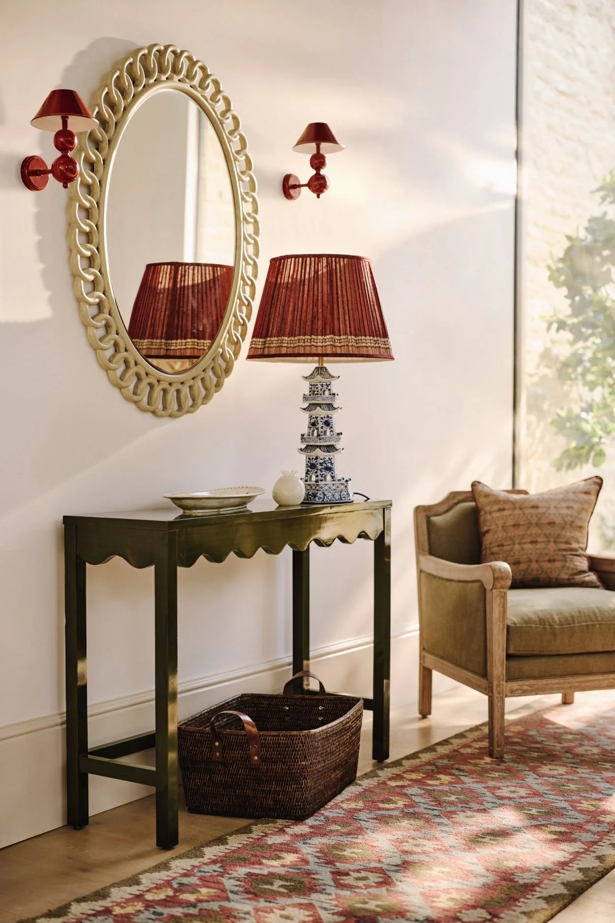 An entryway with a chair console table and mirror above it with two red light fixtures and a lamp with a dark red shade