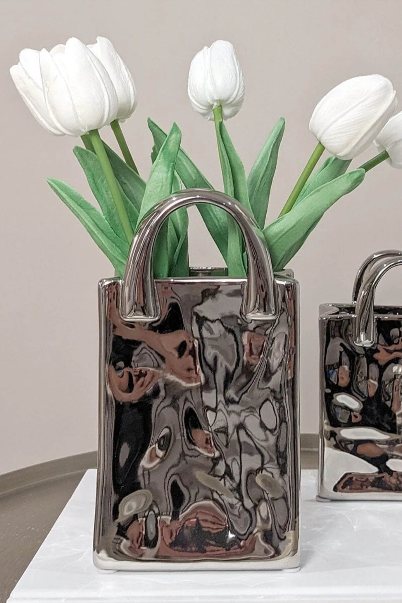 Silver handbag-shaped vase filled with a generous arrangement of flowers and foliage.
