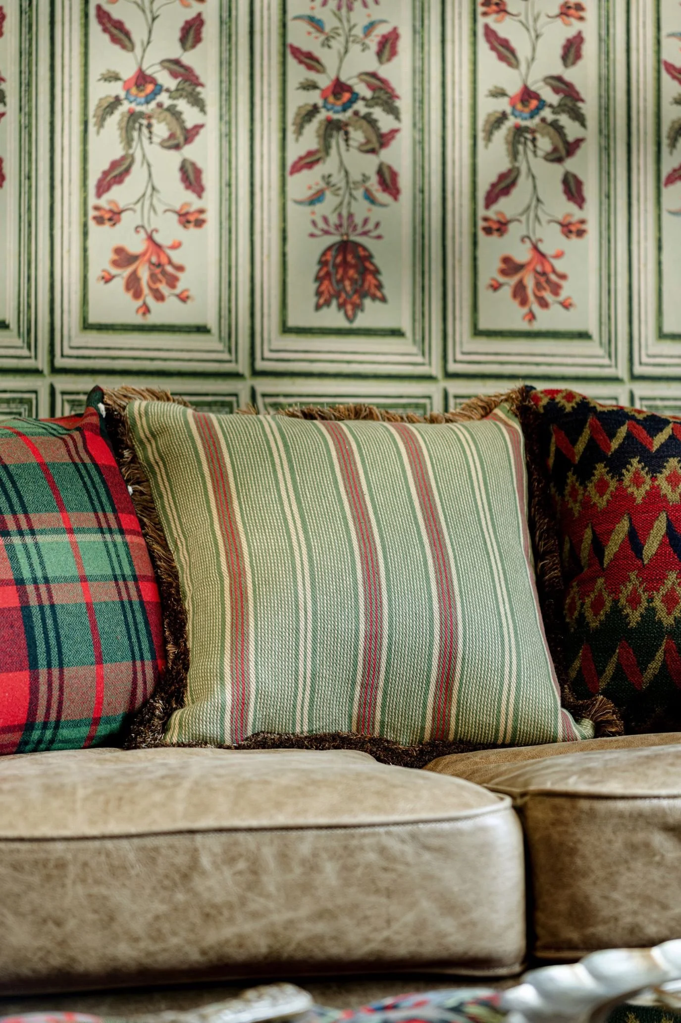 Green striped cushion with decorative edging on a velvet sofa alongside tartan and patterned cushions.