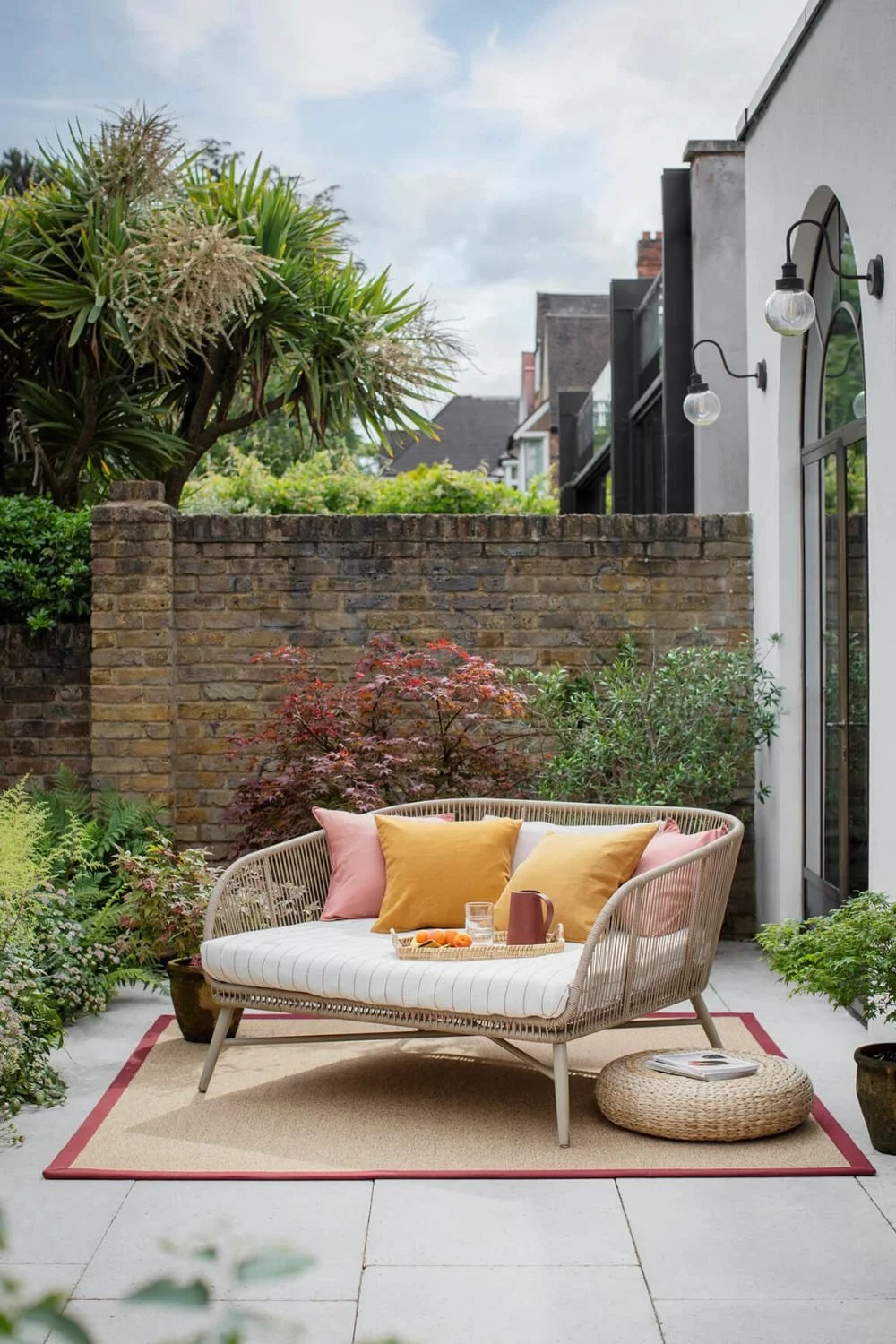 an outdoor terrace with a jute rug with a pink border and an extra larger wicker garden seat with yellow and pink cushions