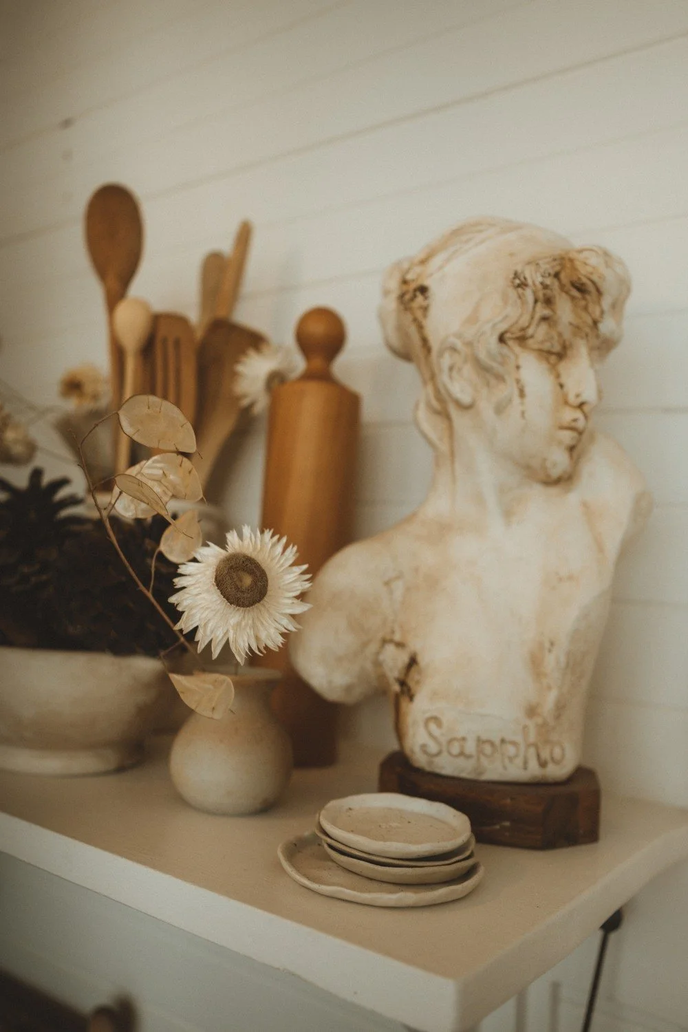 A bust styled on a kitchen shelf with vintage utensils and dried flowers