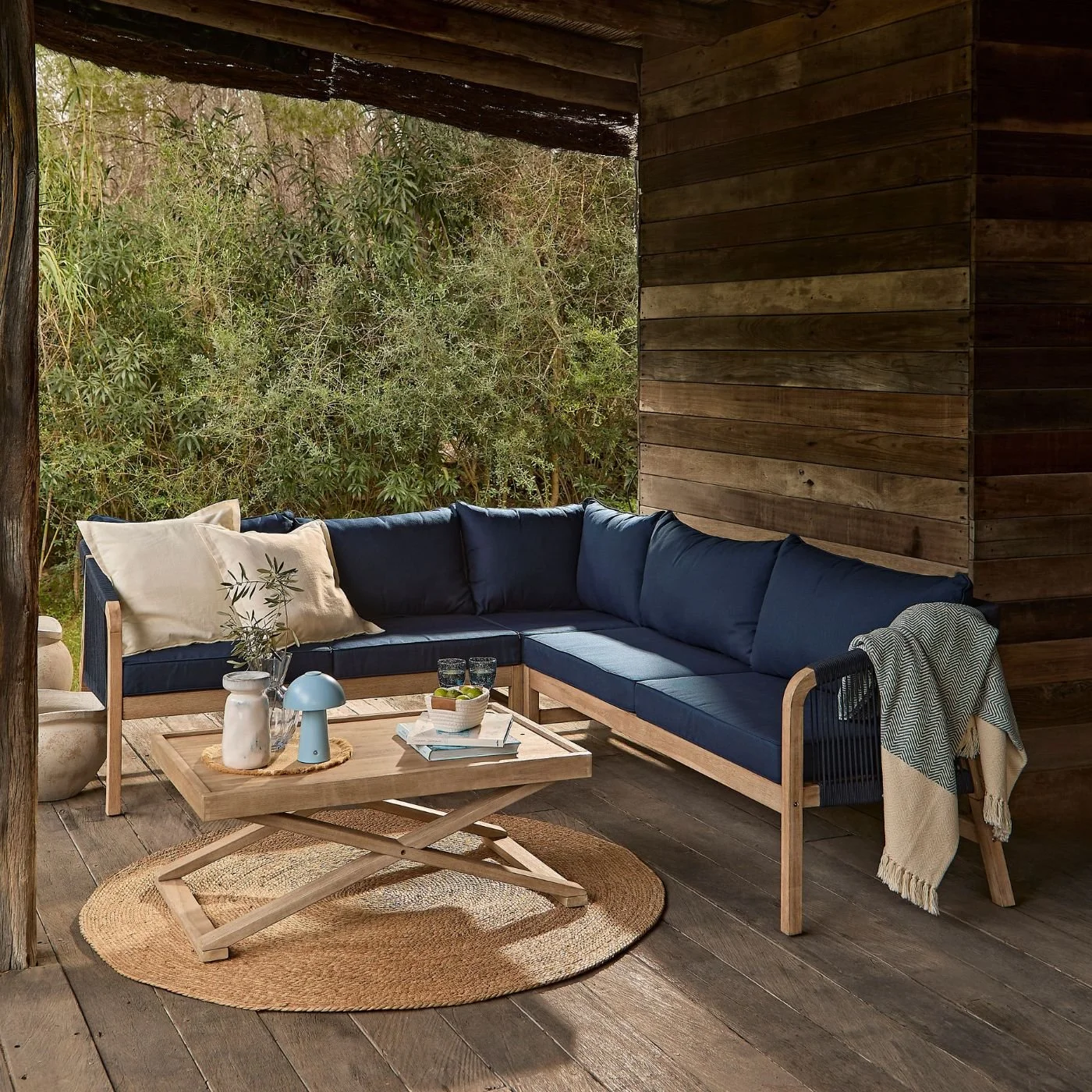 A navy corner sofa with a wooden base in an undercover area with view to the garden