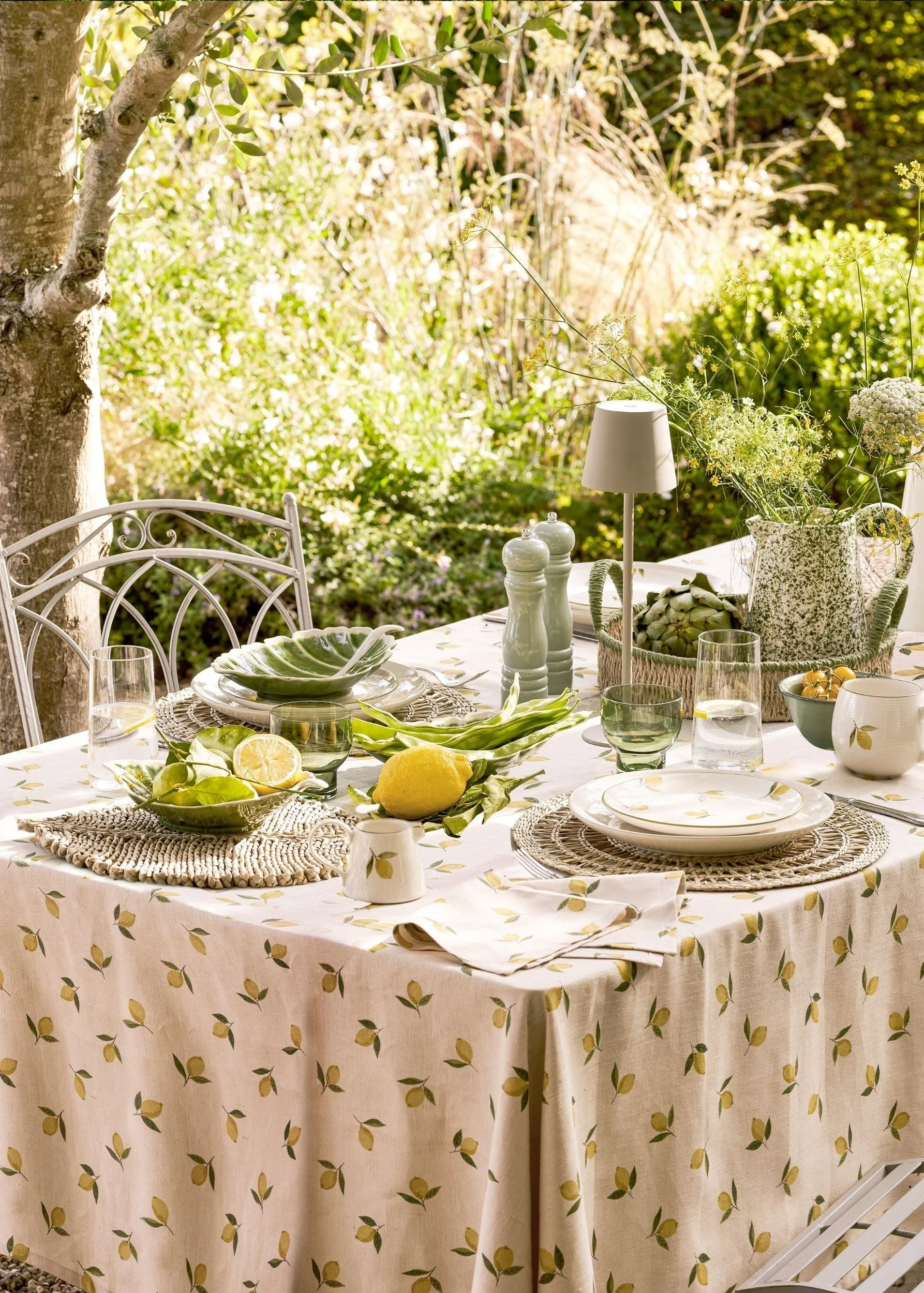 An outdoor table with a cloth with lemons on and matching napkins and crockery