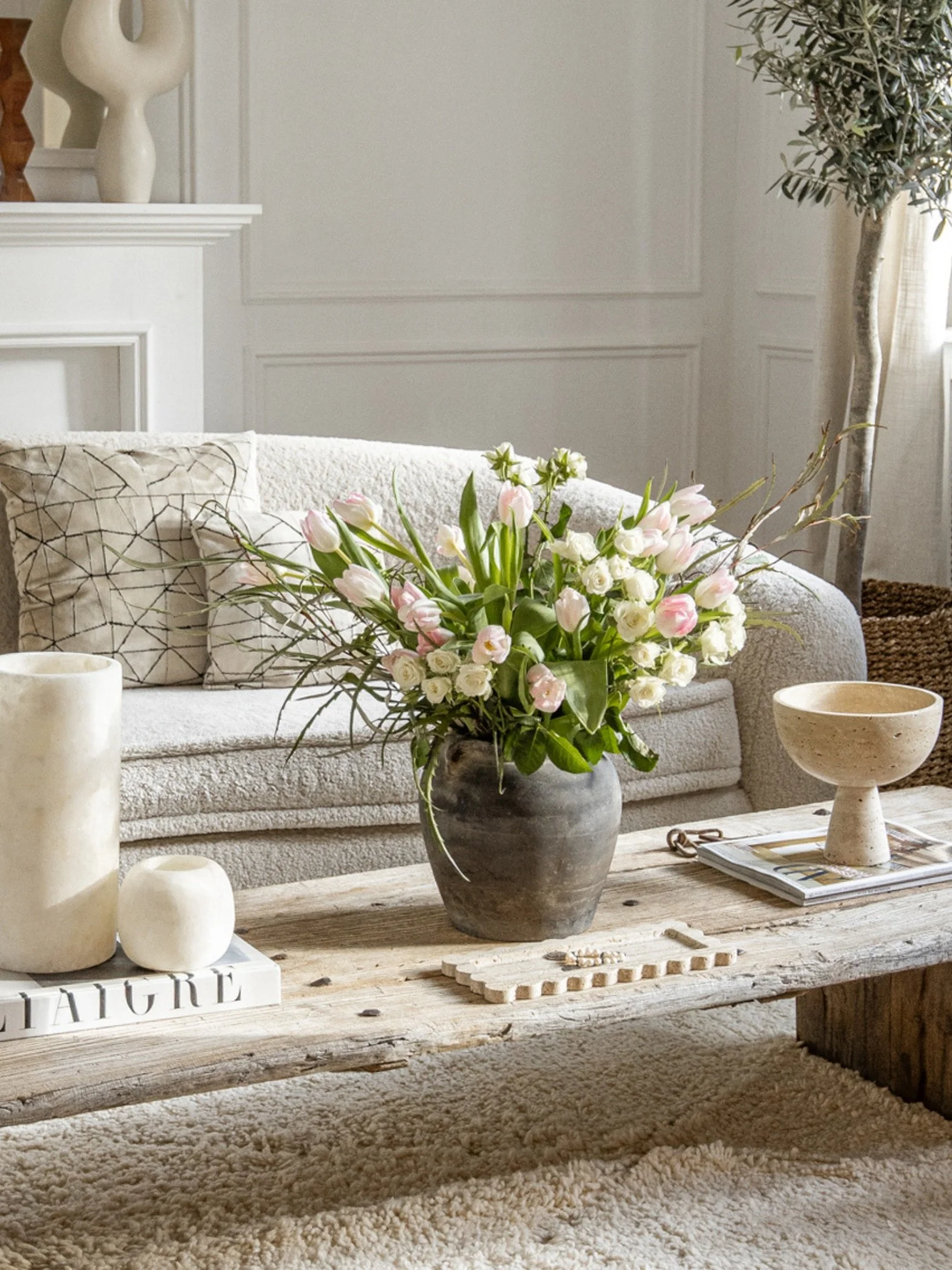 Pink tulips in an antique vase on a wooden coffee table next to books and candle holders